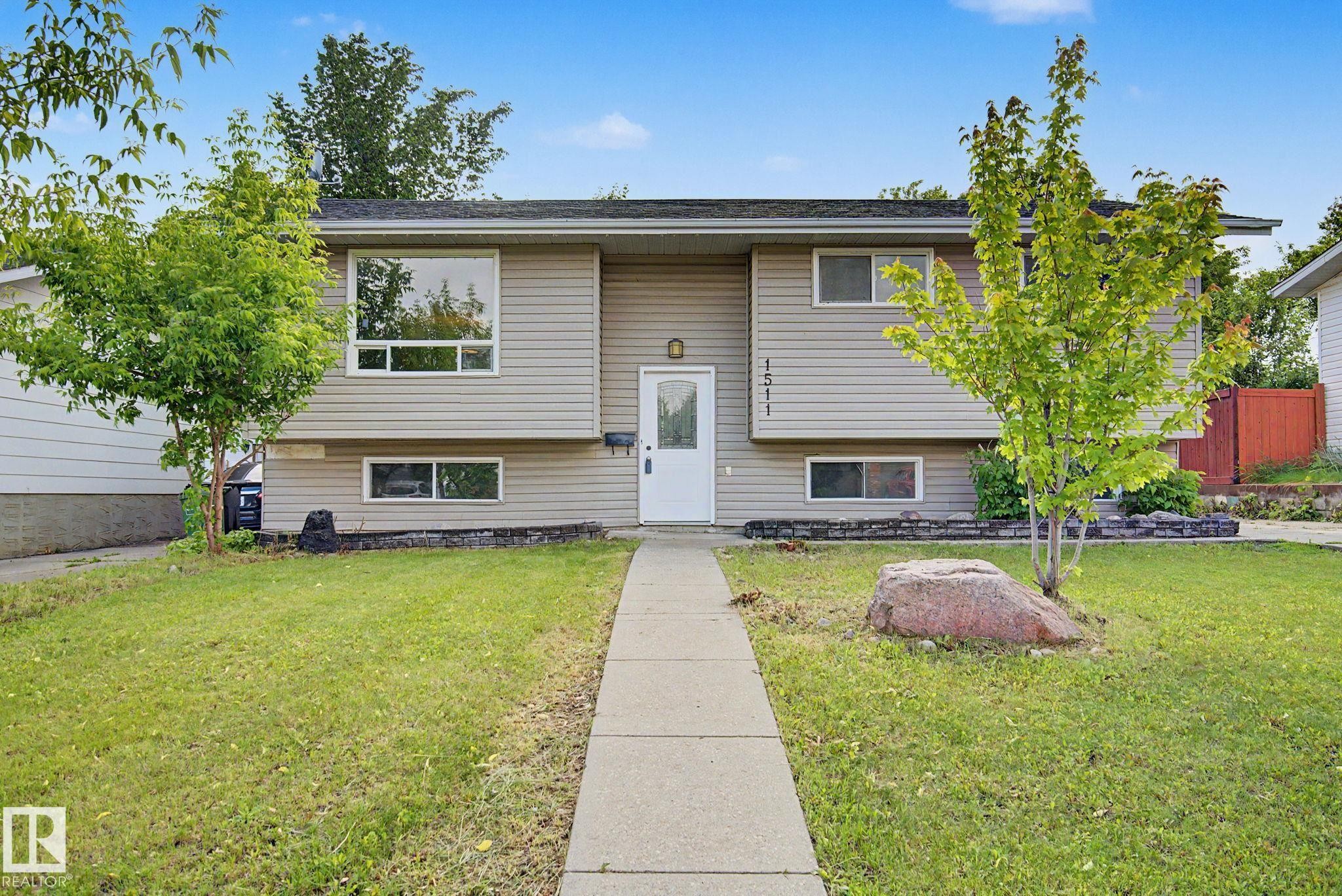 Split-level residence featuring light-toned horizontal siding, a central white entry door, and a concrete pathway - 1511 75 Street, Edmonton, AB