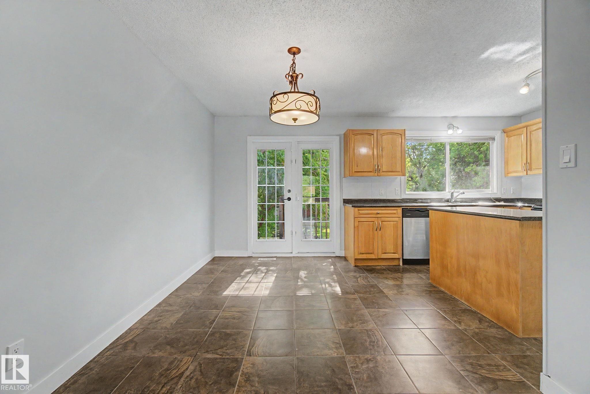 Kitchen area featuring wood cabinetry, dark countertops, a stainless-steel dishwasher, and a double-basin sink under a window - 1511 75 Street, Edmonton, AB