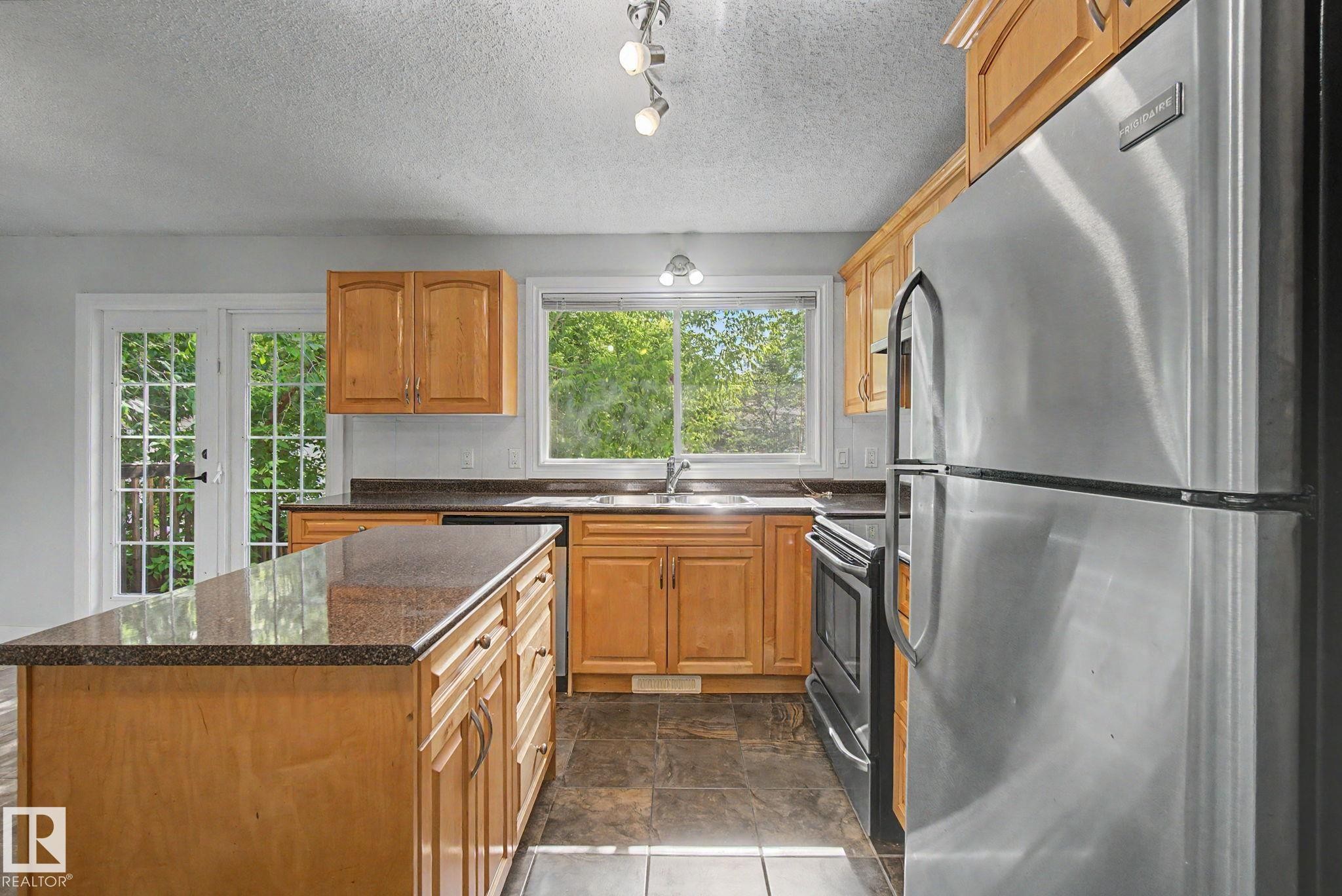 Kitchen featuring wood cabinetry, granite-finish countertops, stainless steel appliances, and tile flooring - 1511 75 Street, Edmonton, AB
