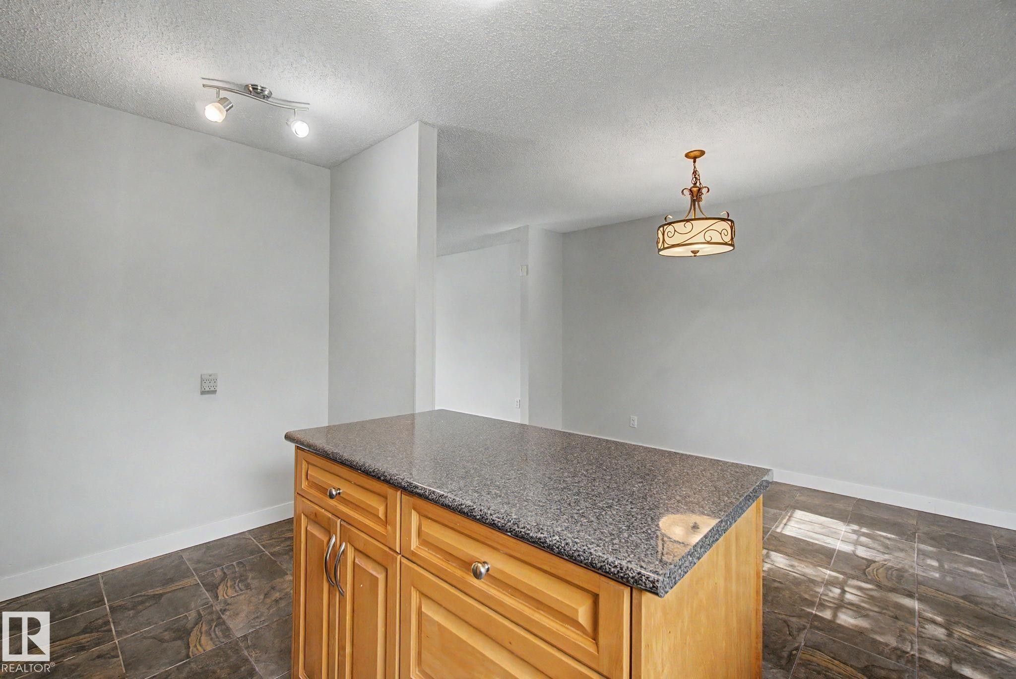 Central kitchen island with wood-finish cabinetry and a speckled countertop - 1511 75 Street, Edmonton, AB