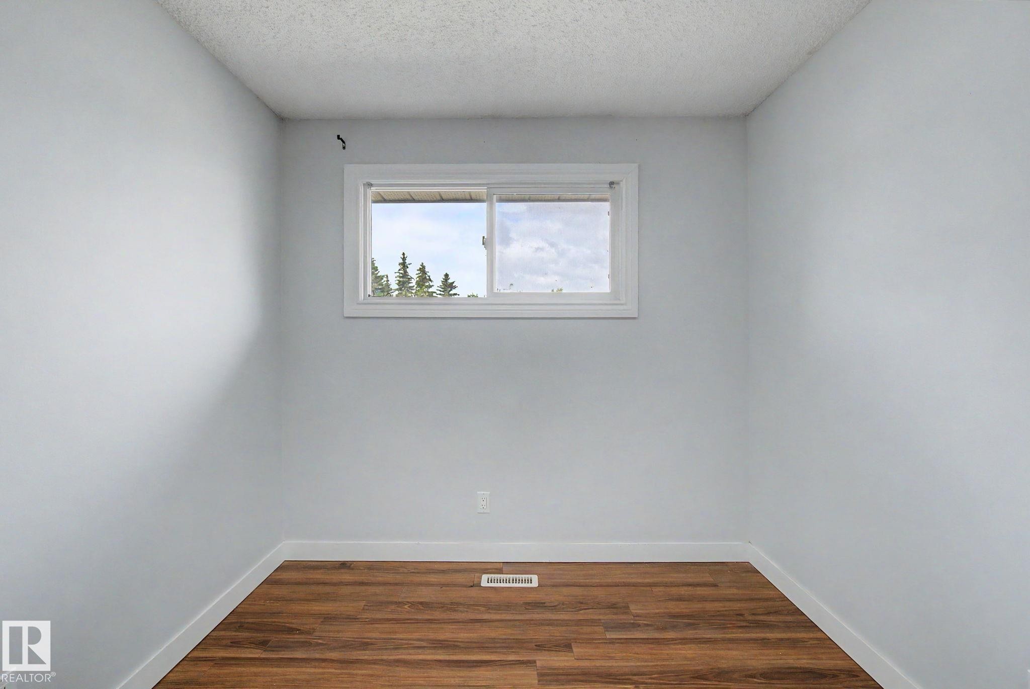 Bright interior room featuring a white-framed window, wood-finish flooring, white baseboards, and light-colored walls - 1511 75 Street, Edmonton, AB