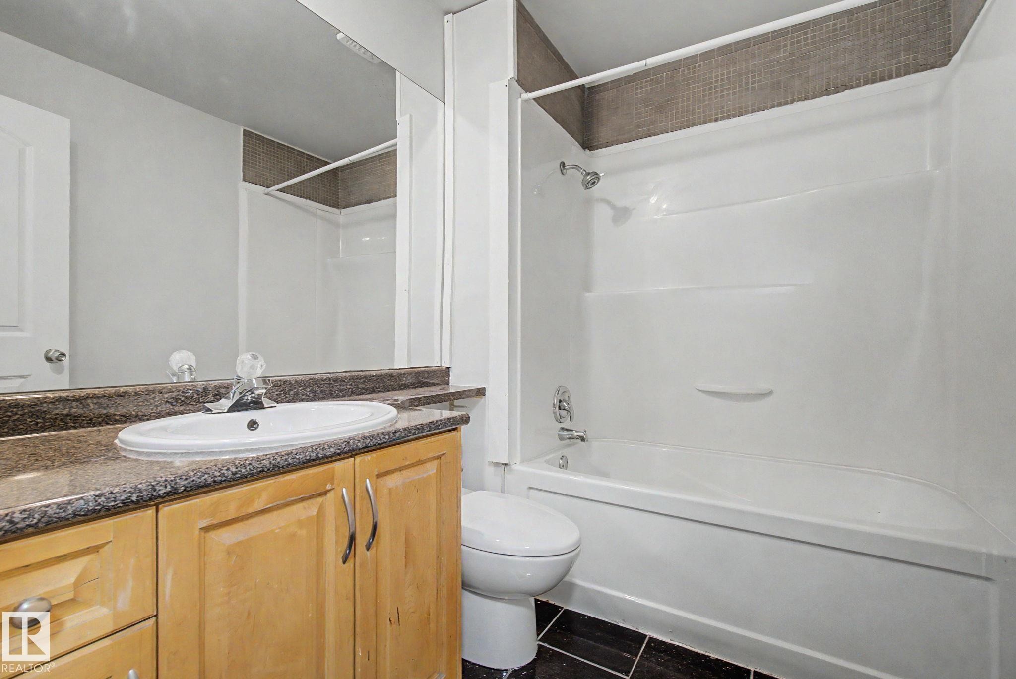 Bathroom featuring a vanity with light wood-finish cabinetry, a white oval sink, and a speckled countertop - 1511 75 Street, Edmonton, AB