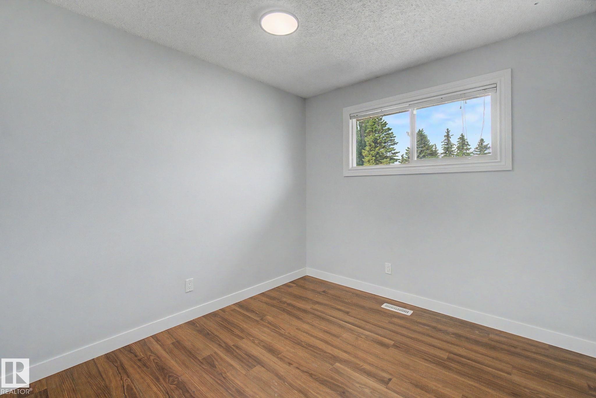 Room featuring a horizontal window, wood-finish flooring, light grey walls, white baseboards, and a recessed ceiling light - 1511 75 Street, Edmonton, AB