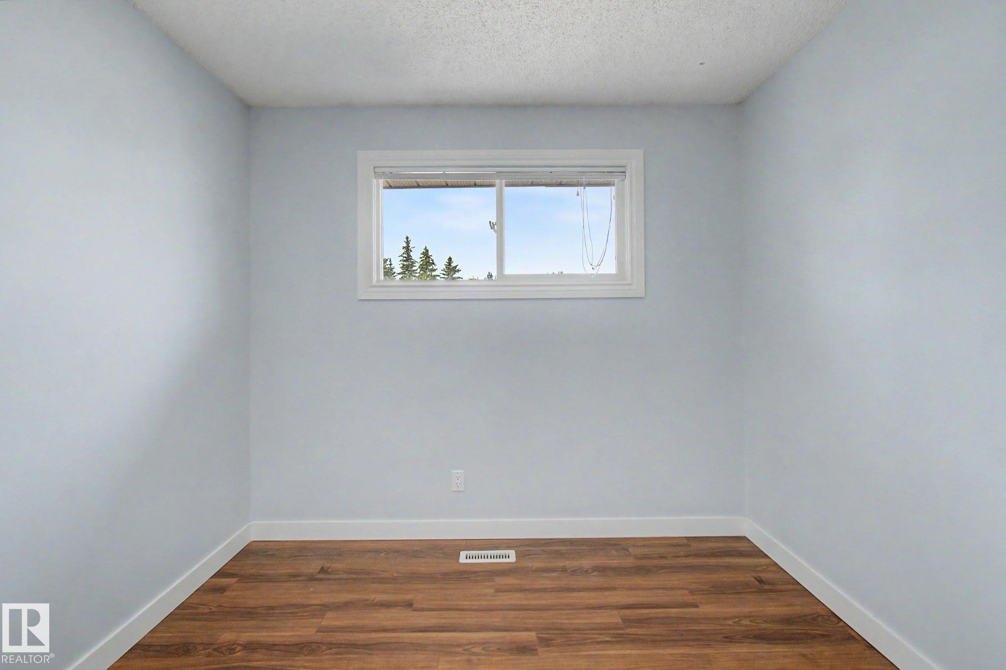 Room featuring wood-finish flooring, light blue wall paint, white baseboards, and a window with white trim - 1511 75 Street, Edmonton, AB
