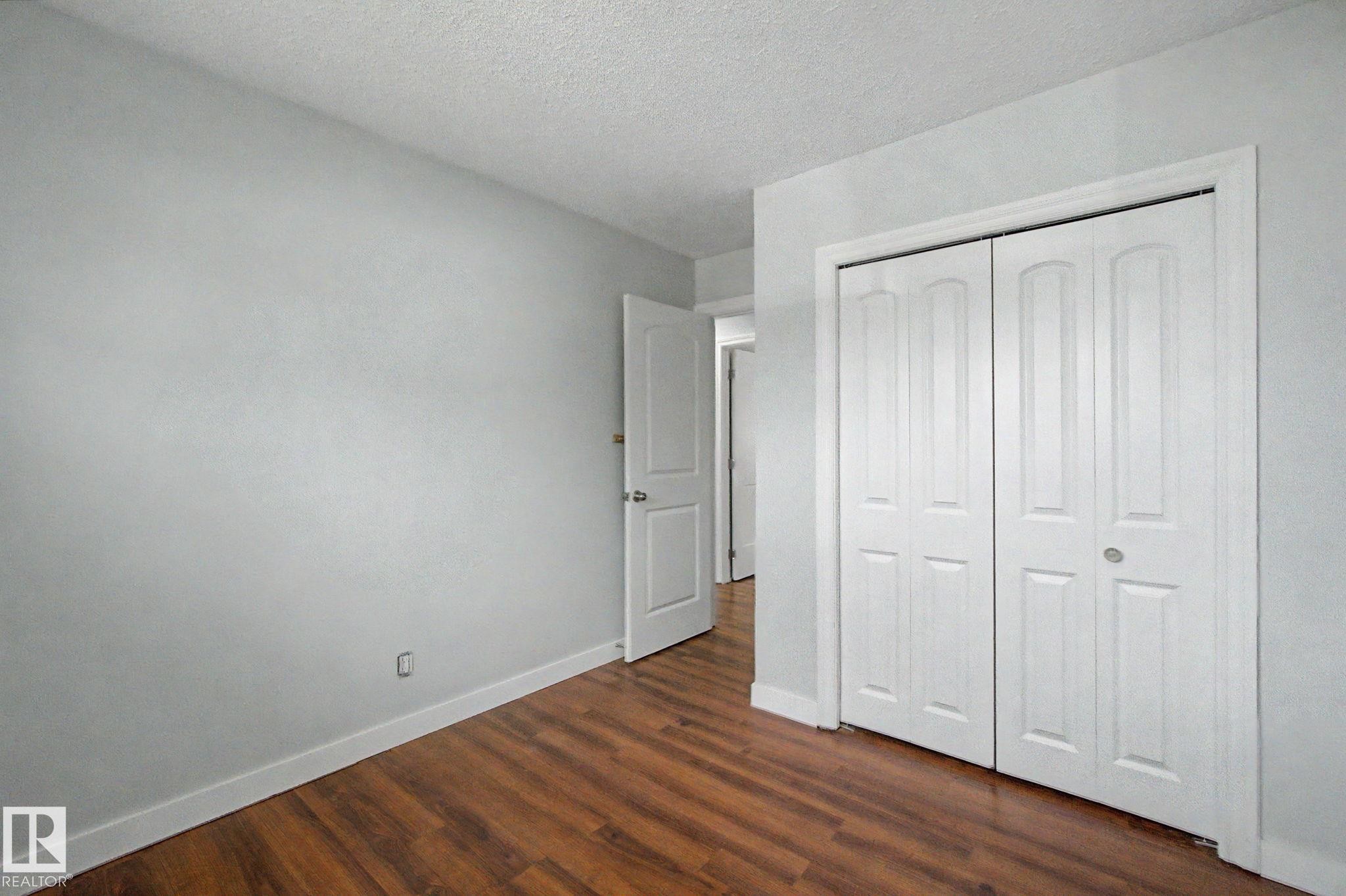 Room featuring wood-finish flooring, light gray walls, white baseboards, and a white bi-fold closet door - 1511 75 Street, Edmonton, AB