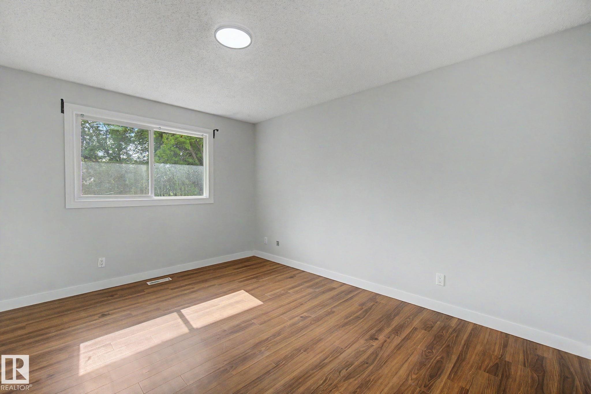 Room featuring wood-finish flooring, light grey walls, and white baseboards - 1511 75 Street, Edmonton, AB