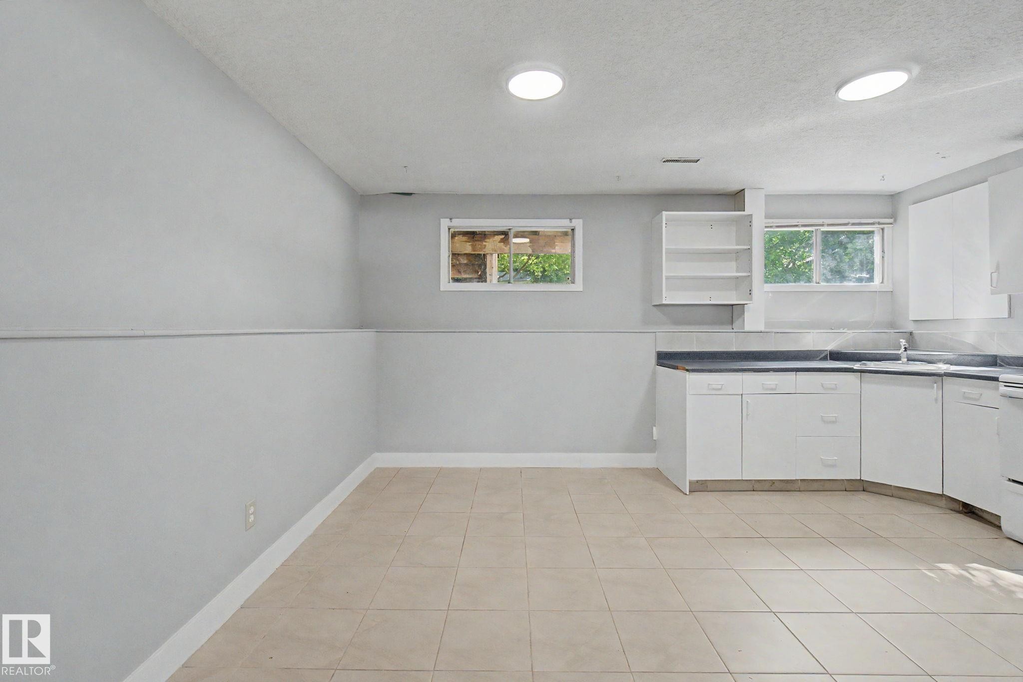 Kitchenette featuring white cabinetry, dark countertops, a stainless steel sink, and ceramic tile flooring - 1511 75 Street, Edmonton, AB