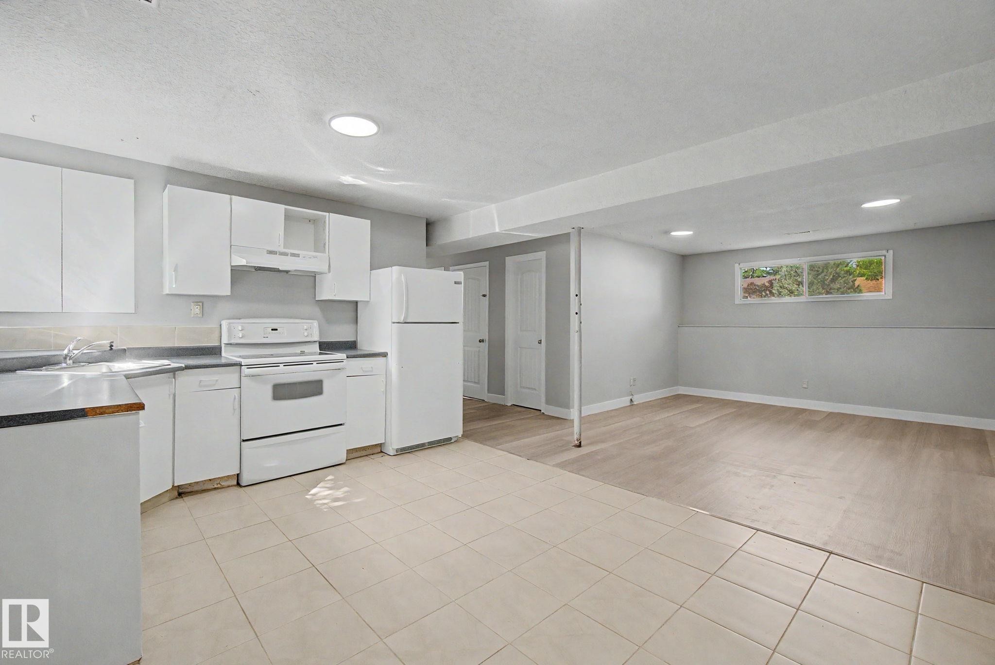 Kitchen and living area featuring white cabinetry, a white appliance suite, light-toned tile flooring, recessed lighting, and a large window - 1511 75 Street, Edmonton, AB