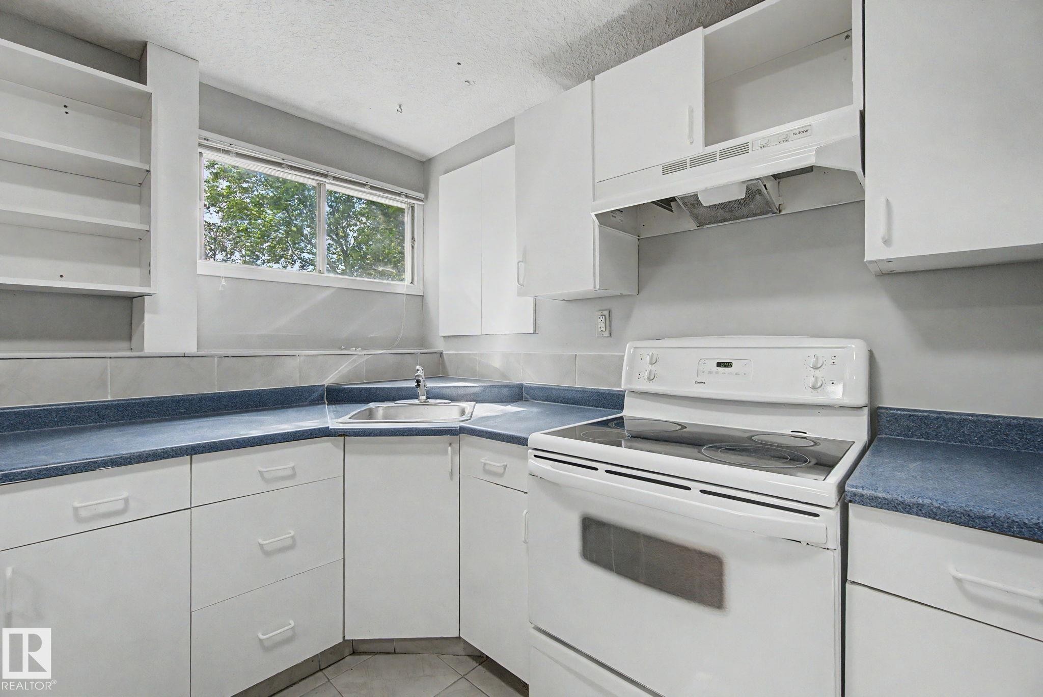 Kitchen featuring white cabinetry, blue countertops, a stainless steel sink, a white electric range with a matching range hood, and tile flooring - 1511 75 Street, Edmonton, AB