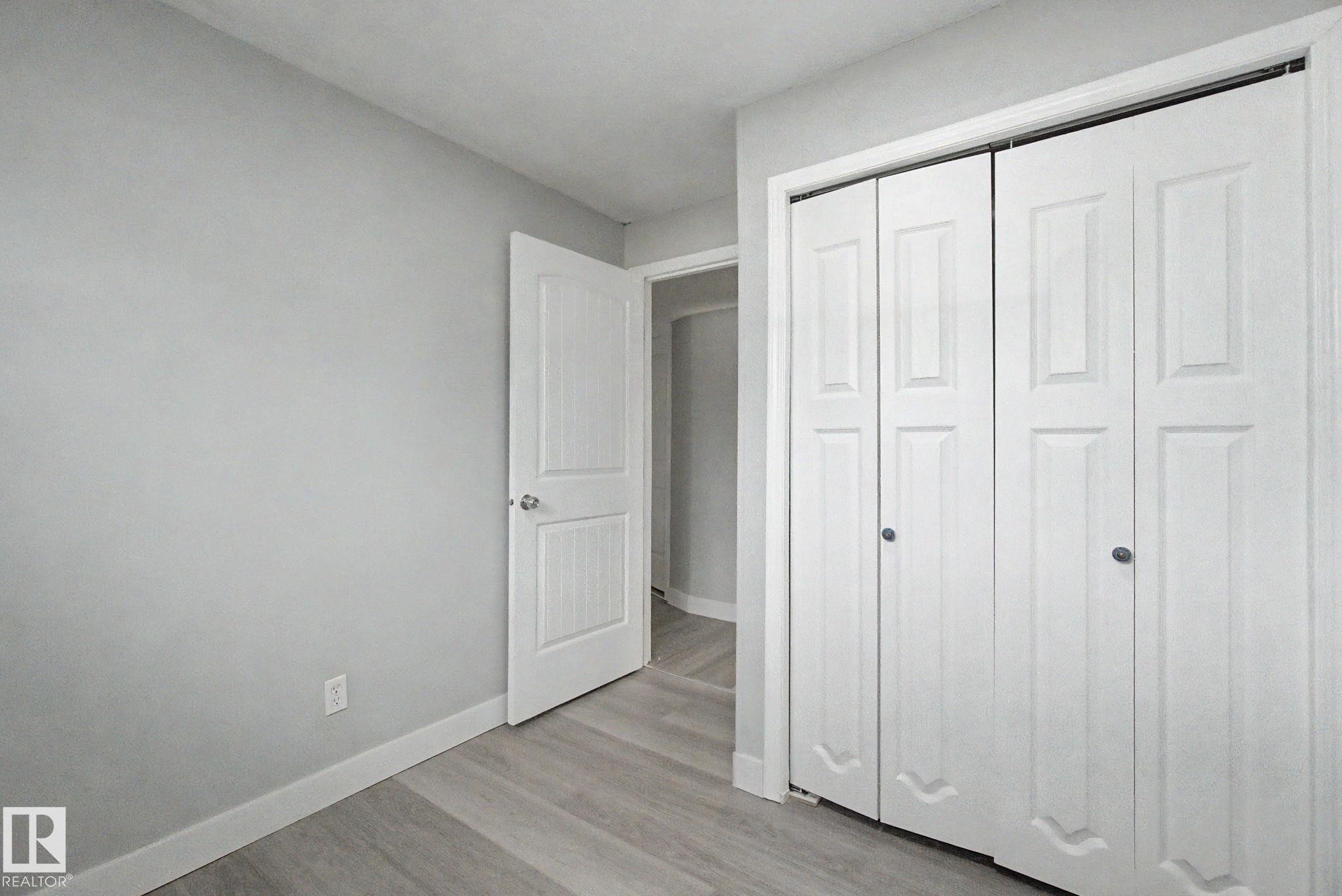Bedroom featuring light gray wall paint, wood-finish flooring, white baseboards, and a bi-fold closet - 1511 75 Street, Edmonton, AB