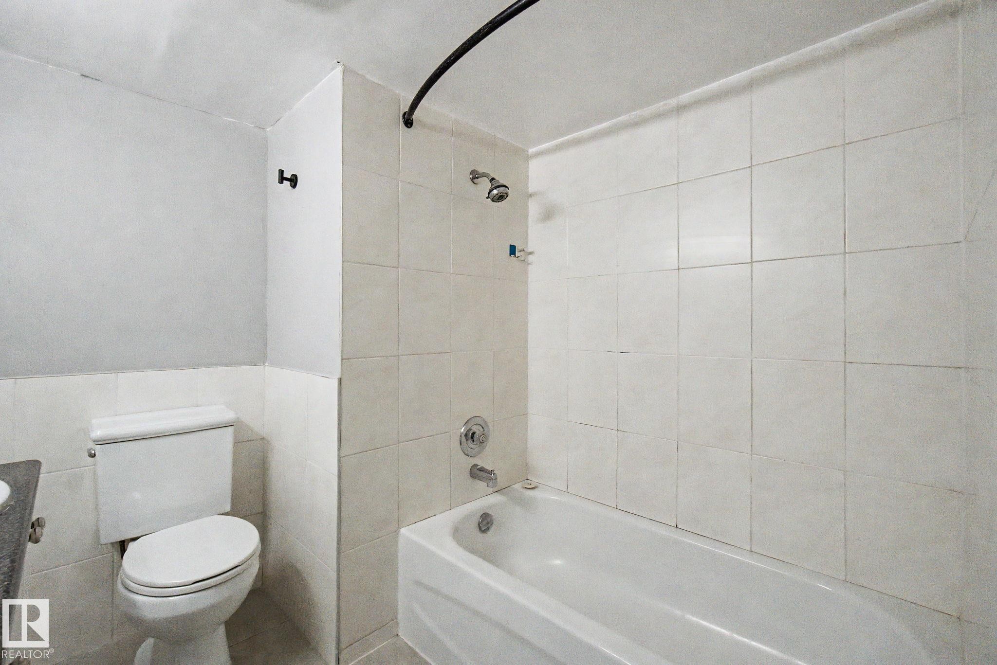 Bathroom featuring a white bathtub, ceramic tile shower surround, and a standard toilet - 1511 75 Street, Edmonton, AB
