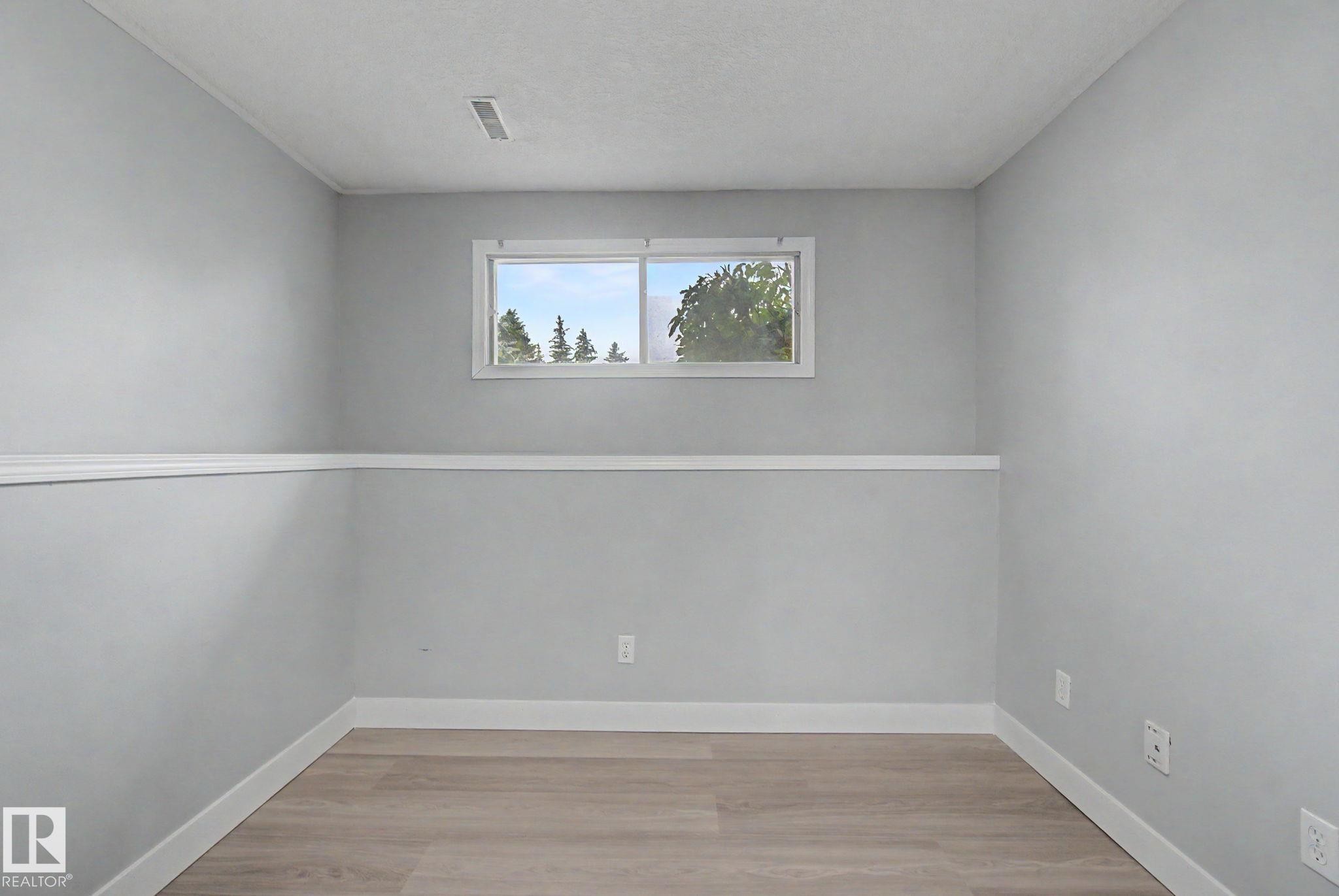 Room featuring wood-finish flooring, light grey walls with white chair rail molding, and a white-framed window - 1511 75 Street, Edmonton, AB