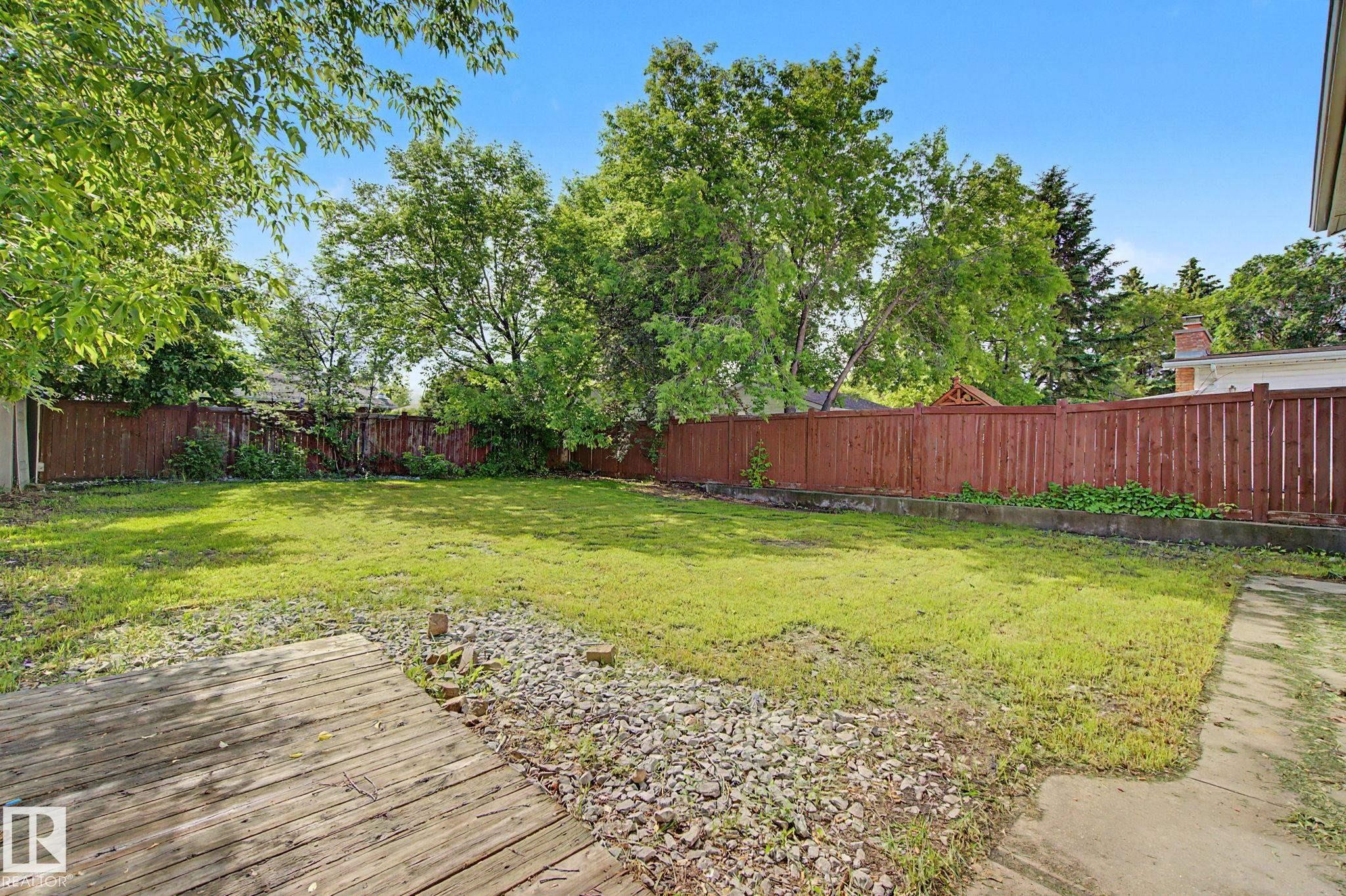 Expansive backyard featuring a lush lawn, mature trees, a wooden privacy fence, and a wooden deck - 1511 75 Street, Edmonton, AB
