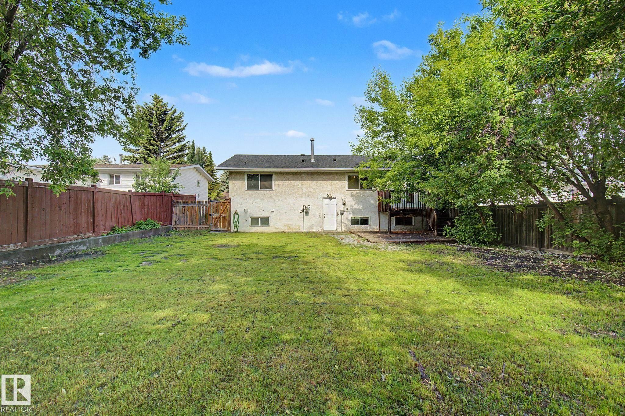 Expansive backyard featuring a large grassy area, a multi-level deck, and mature perimeter trees - 1511 75 Street, Edmonton, AB