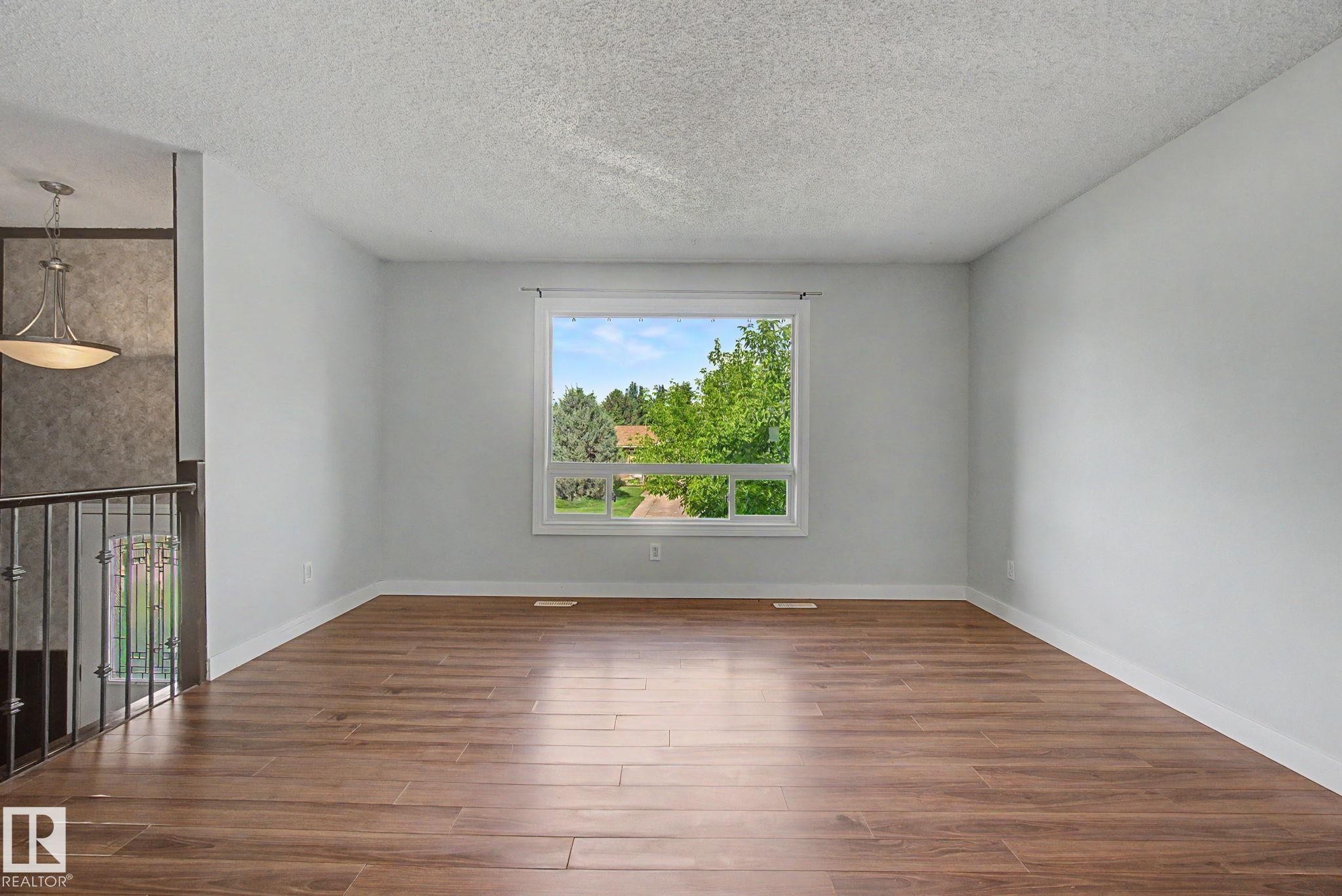 Spacious room featuring wood-finish flooring, white baseboards, and light gray walls - 1511 75 Street, Edmonton, AB