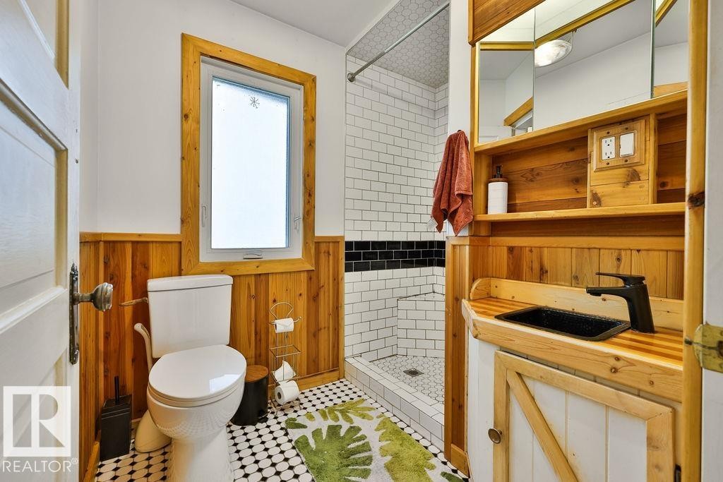Bathroom featuring wood-paneled wainscoting, a white toilet, and a window with wood trim - 8318 80 Avenue, Edmonton, AB