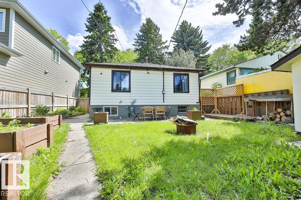 Rear exterior featuring white horizontal siding, black-framed windows, and a concrete patio - 8318 80 Avenue, Edmonton, AB
