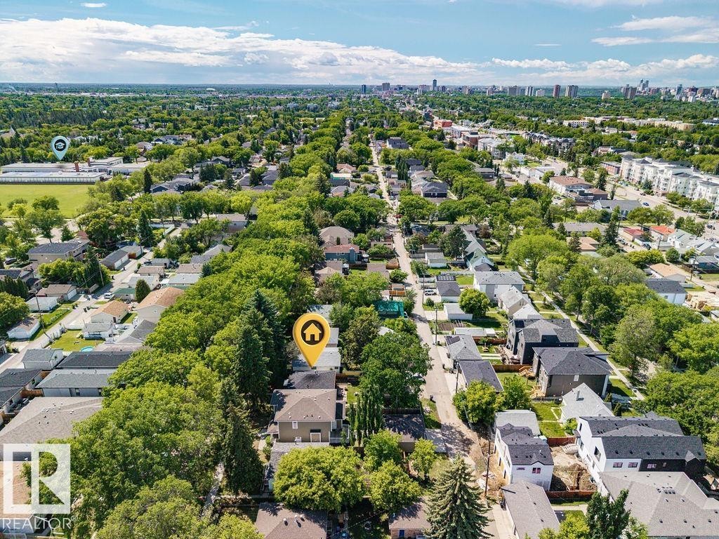 Aerial perspective of a residential neighborhood featuring tree-lined streets, a distant urban skyline, and a mix of single-family homes and multi-story buildings - 8318 80 Avenue, Edmonton, AB