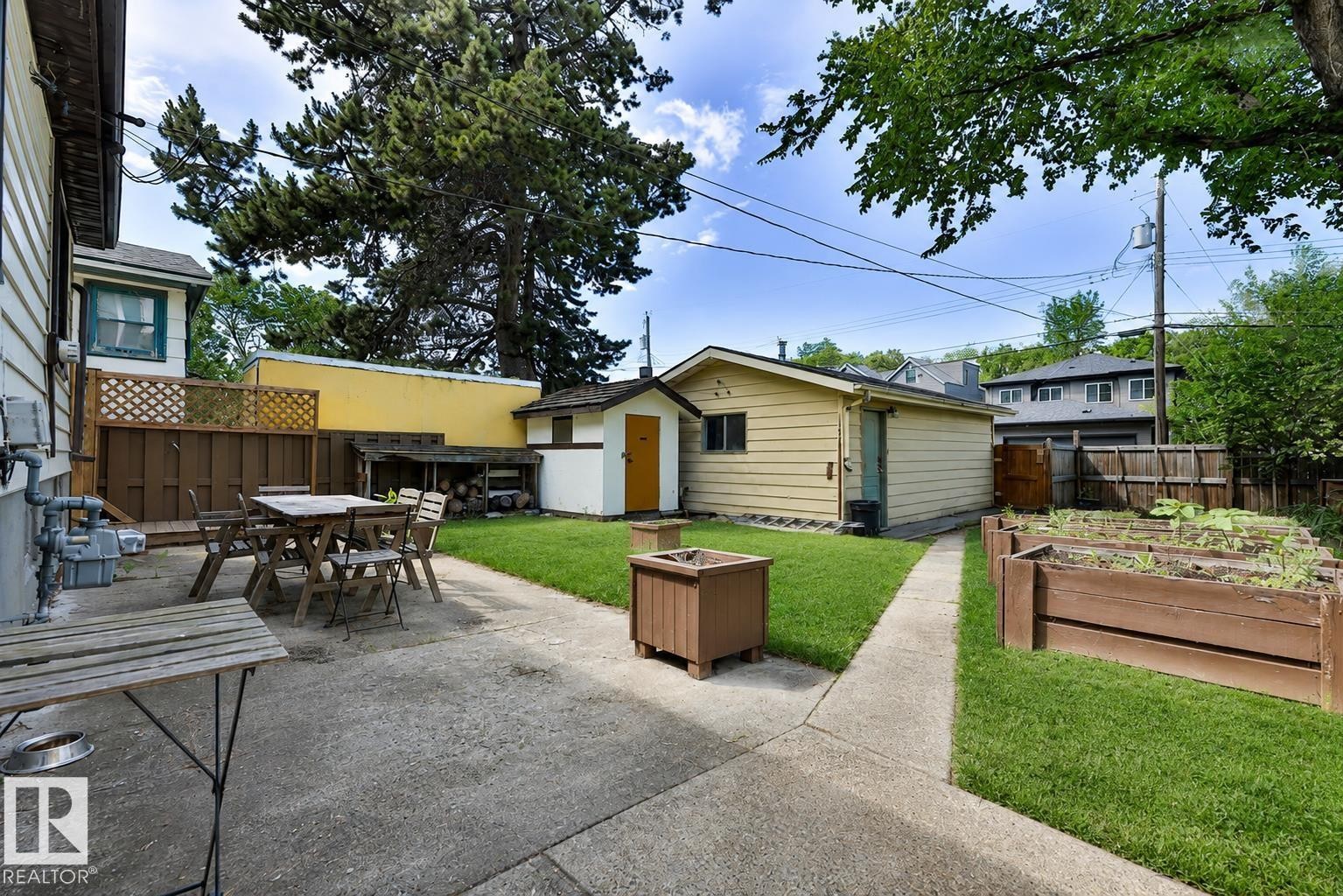 Expansive backyard featuring a concrete patio, grassy lawn, raised garden beds, a detached garage, and a separate storage shed - 8318 80 Avenue Nw, Edmonton, AB - Outdoor With Deck Patio Veranda