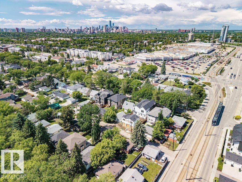Aerial perspective showcasing a residential neighborhood with mature trees, a commercial center, and a distant city skyline - 8318 80 Avenue Nw, Edmonton, AB - Outdoor With View