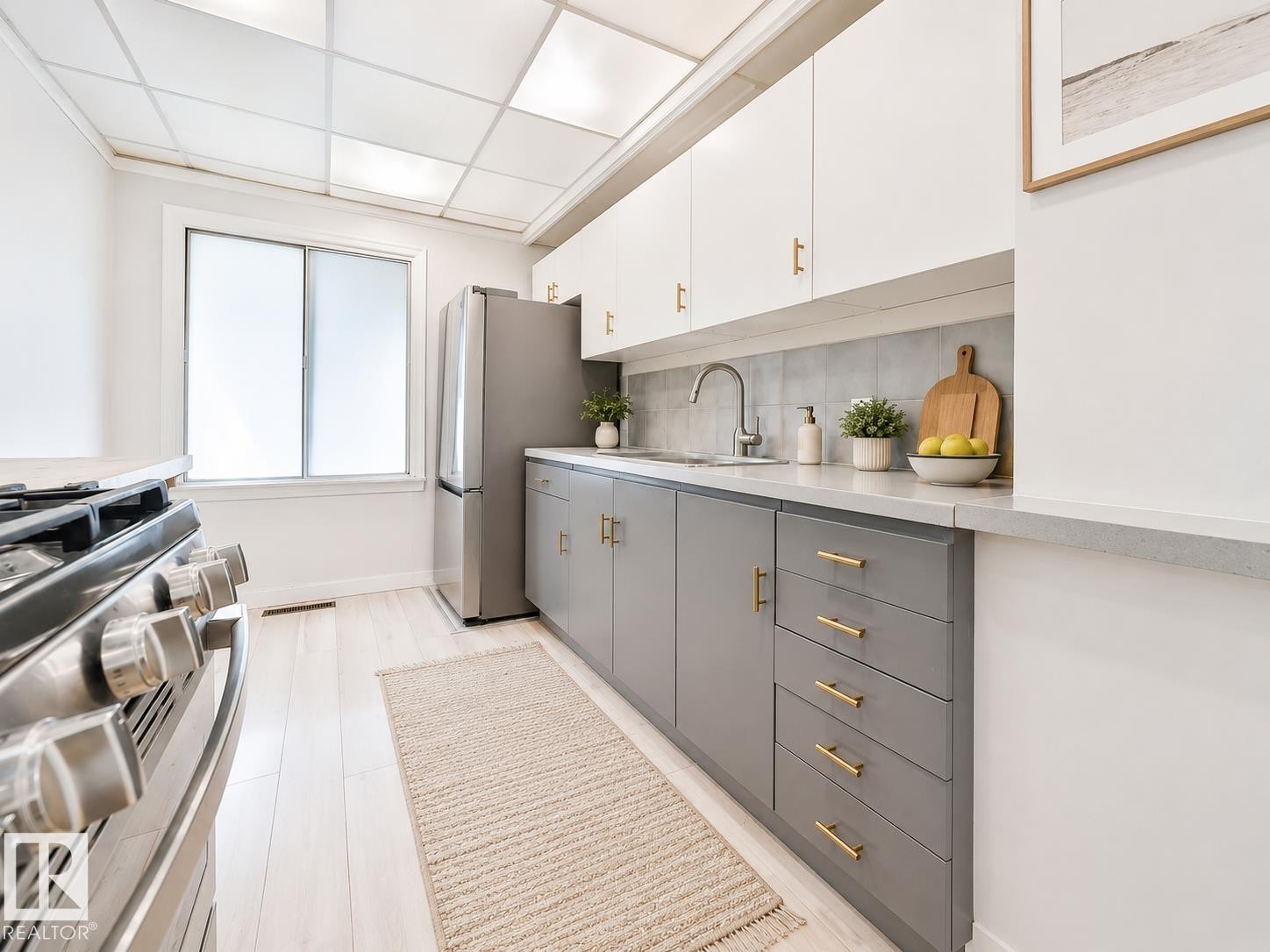 Modern kitchen featuring two-tone cabinetry with gold-tone hardware, a stainless steel gas range, and wood-finish flooring - 8318 80 Avenue, Edmonton, AB