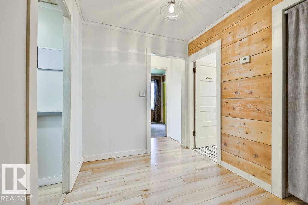 Hallway featuring wood-finish flooring, white painted walls, and a distinctive wood-paneled accent wall - 8318 80 Avenue, Edmonton, AB