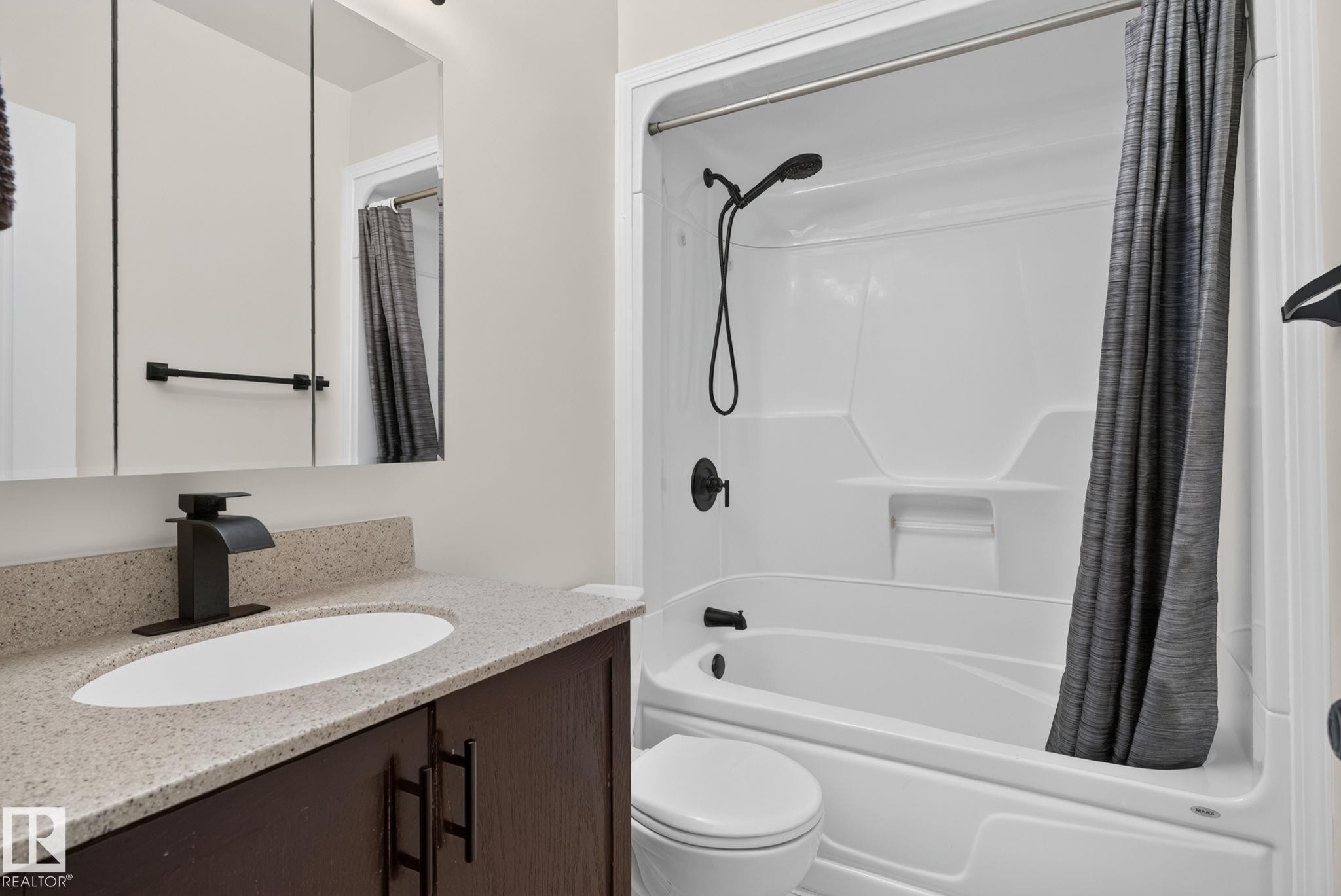 Bathroom featuring a dark wood-finish vanity with a light-toned countertop, an undermount sink, and a black faucet - 12952 114 Street Nw, Edmonton, AB
