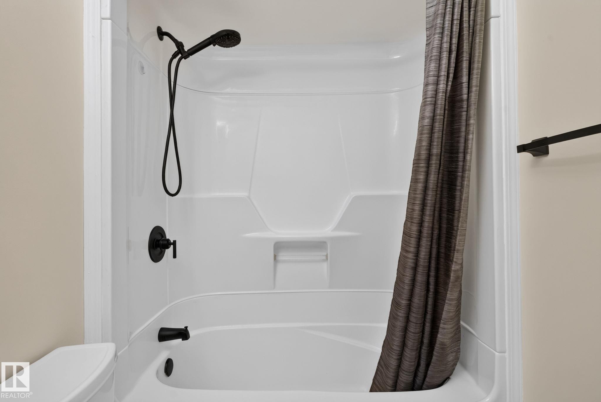 White fiberglass tub and shower combination featuring matte black fixtures, an integrated shelf, and a curved shower rod - 12952 114 Street Nw, Edmonton, AB