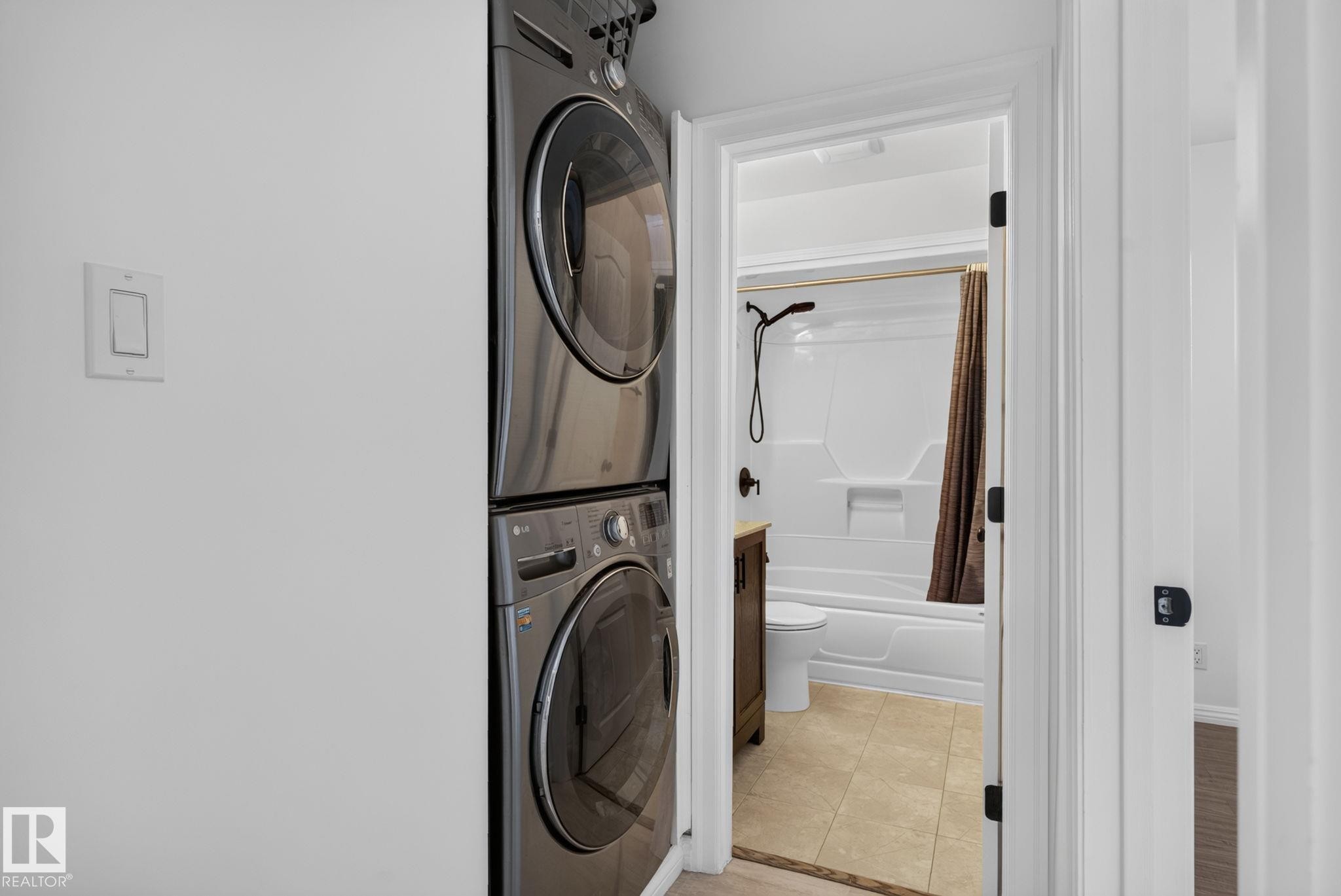 Stackable washer and dryer appliances with a white wall-mounted light switch - 12952 114 Street Nw, Edmonton, AB