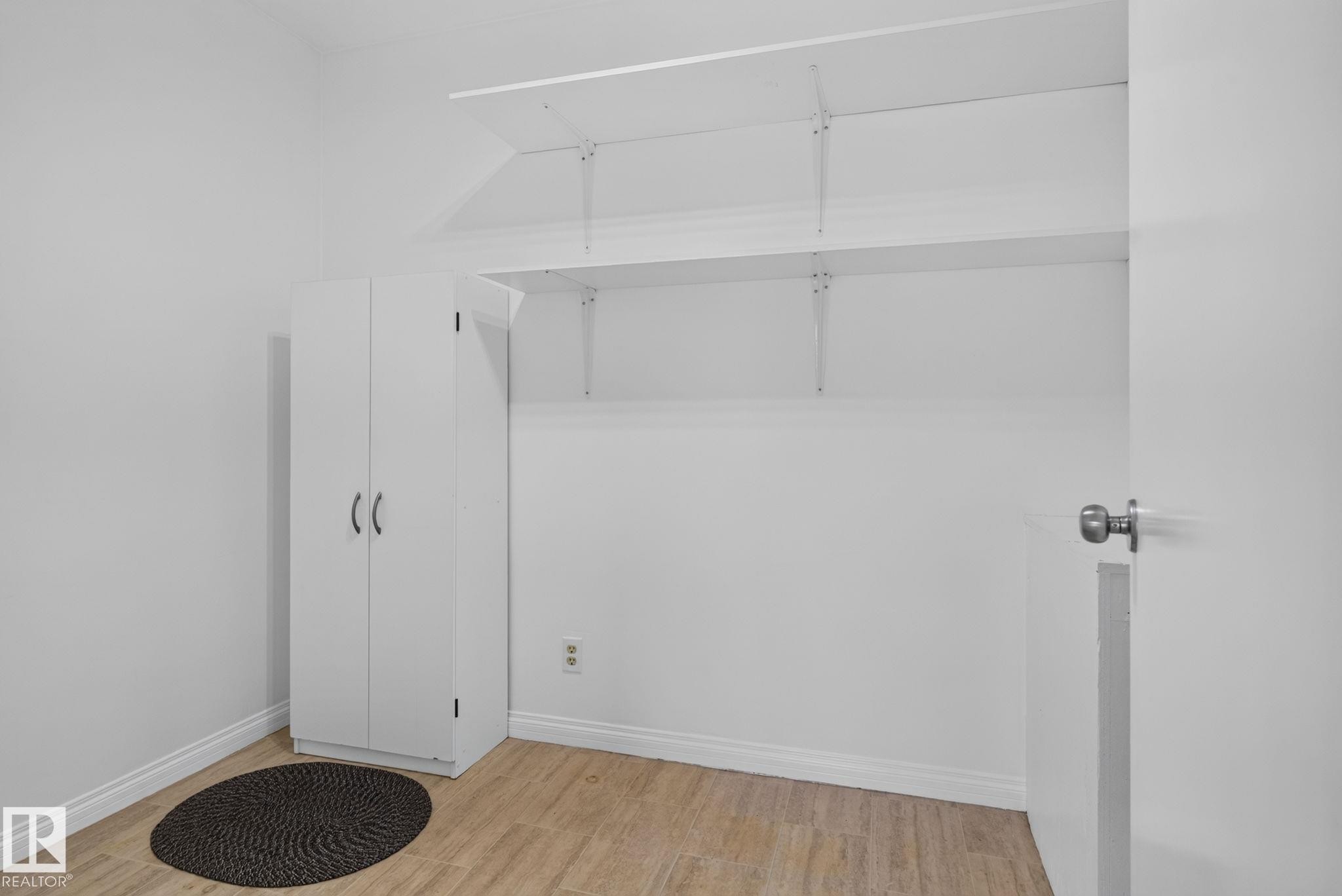 White room featuring built-in shelving, a white storage cabinet with dual doors, and wood-finish flooring - 12952 114 Street Nw, Edmonton, AB - Indoor Photo Showing Other Room