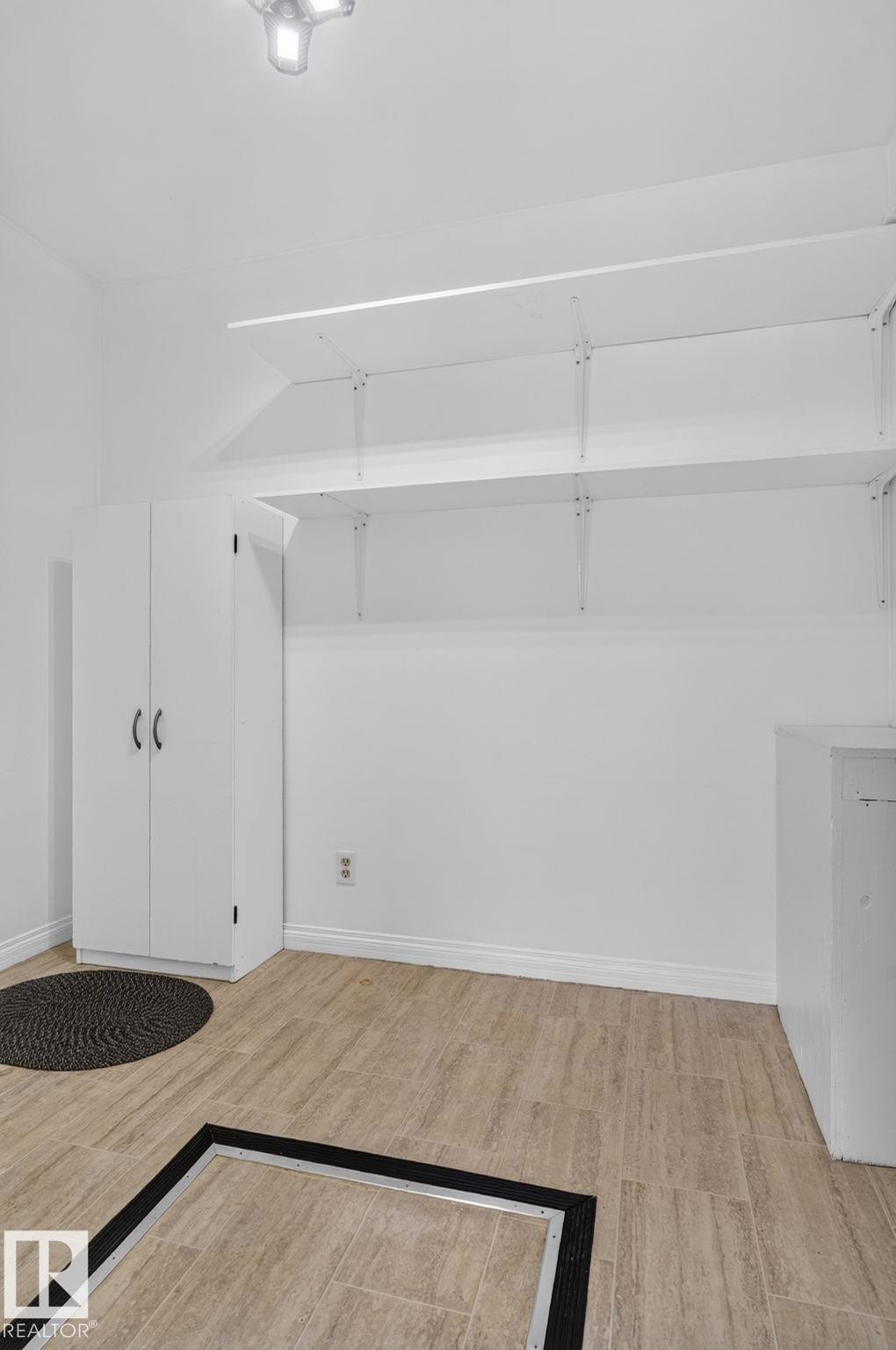 Utility room featuring light-toned tile flooring, white built-in cabinetry, adjustable shelving, and a surface-mounted ceiling light fixture - 12952 114 Street Nw, Edmonton, AB