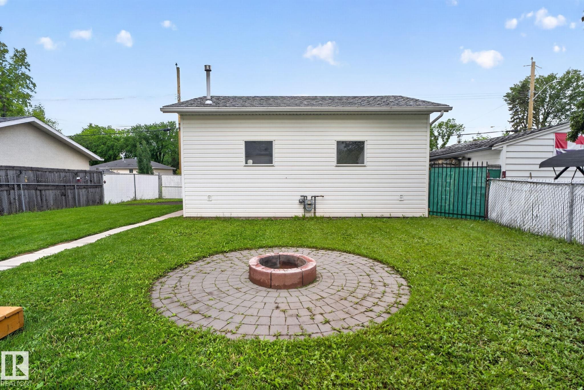 Spacious backyard featuring a circular paver patio with a central fire pit, surrounded by a lawn - 12952 114 Street Nw, Edmonton, AB