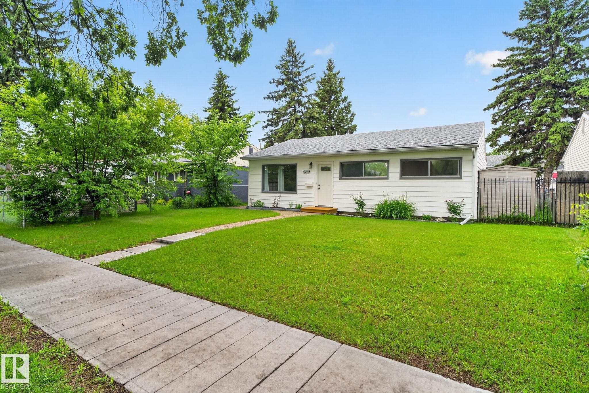 White exterior residence featuring a gray shingle roof, dark-trimmed windows, and a concrete sidewalk - 12952 114 Street Nw, Edmonton, AB