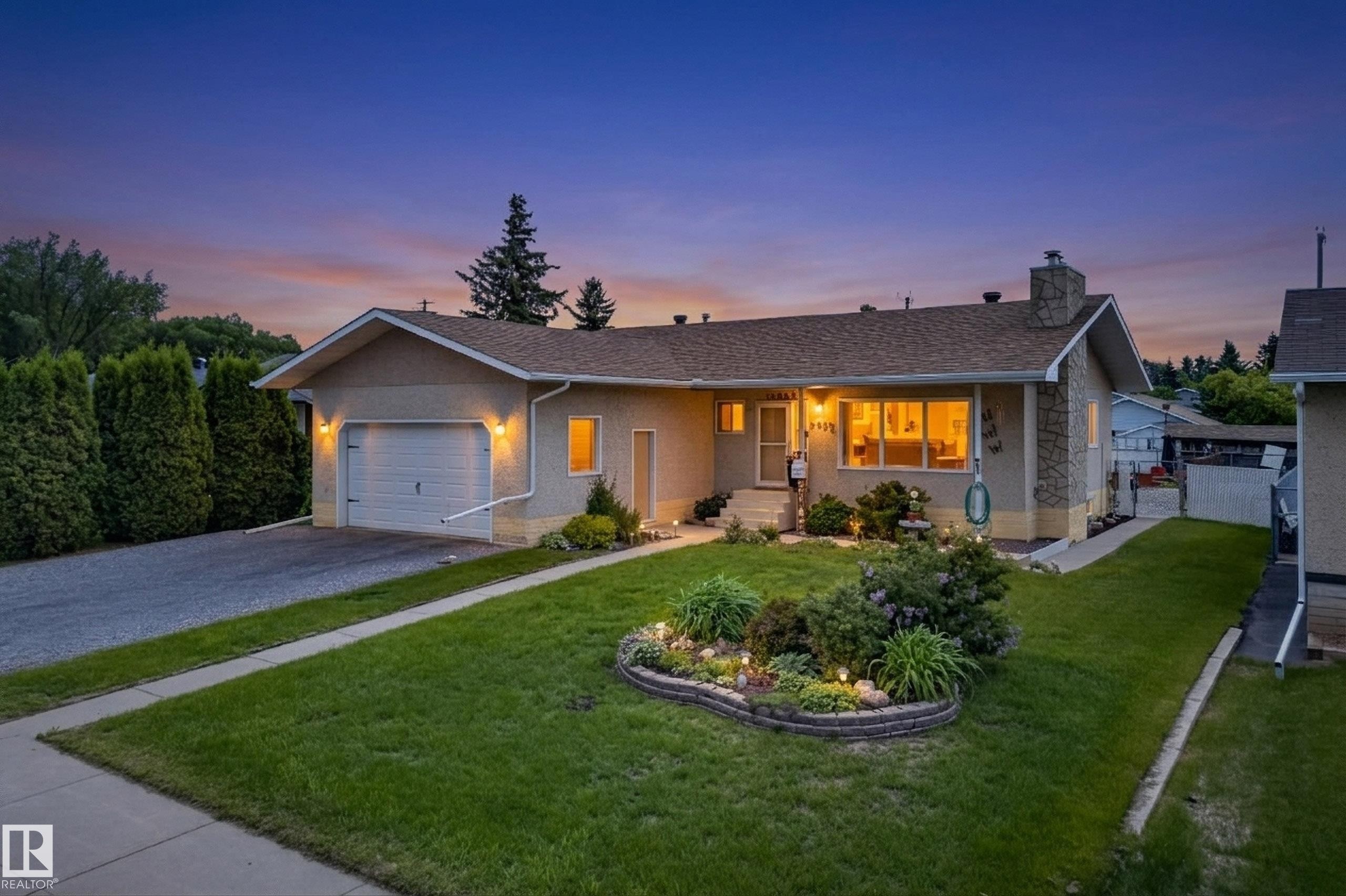 Single-story residence featuring a front yard with manicured lawn and garden bed, an attached garage, a paved driveway, and an exterior stone chimney - 10935 152 Street, Edmonton, AB
