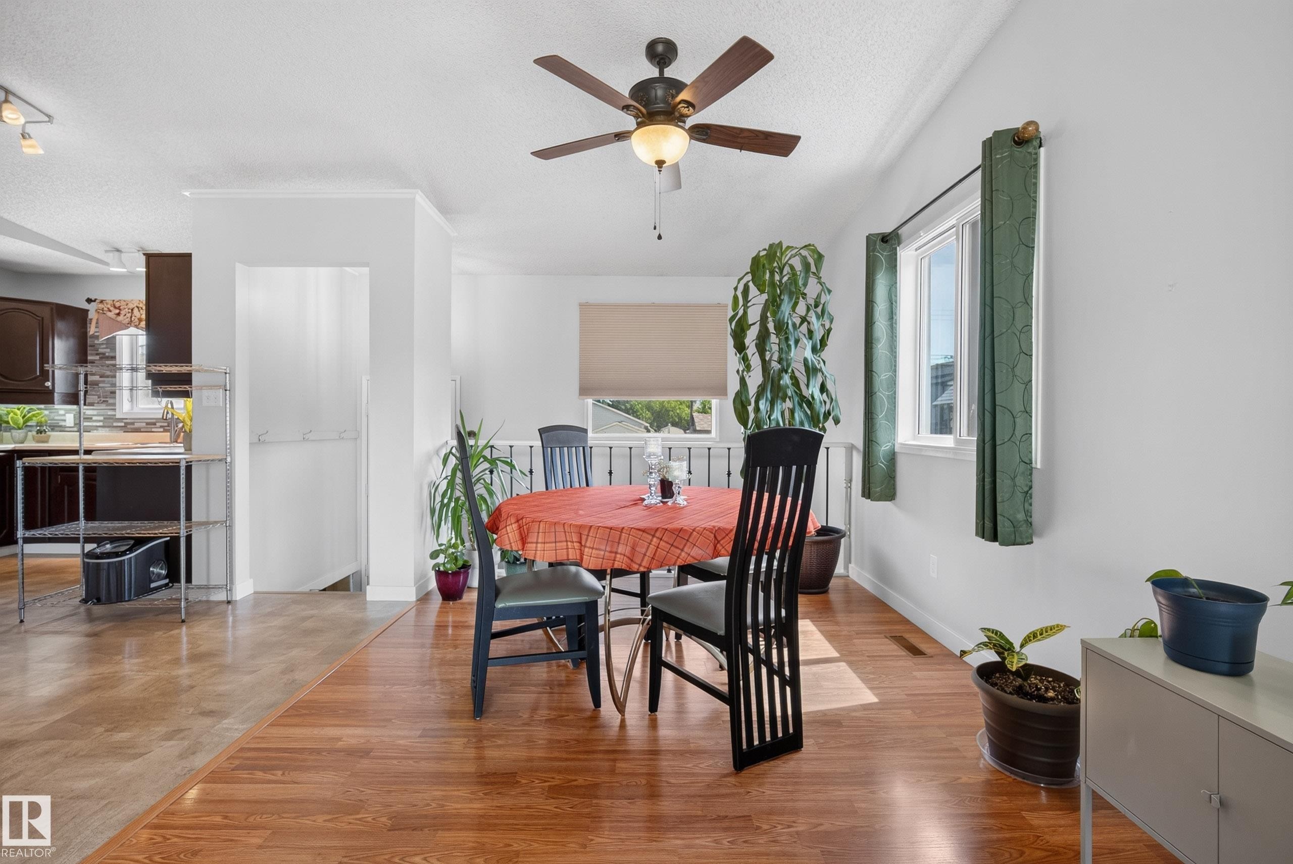 Bright dining area featuring wood-finish flooring, a ceiling fan with integrated lighting, and white walls - 10935 152 Street, Edmonton, AB