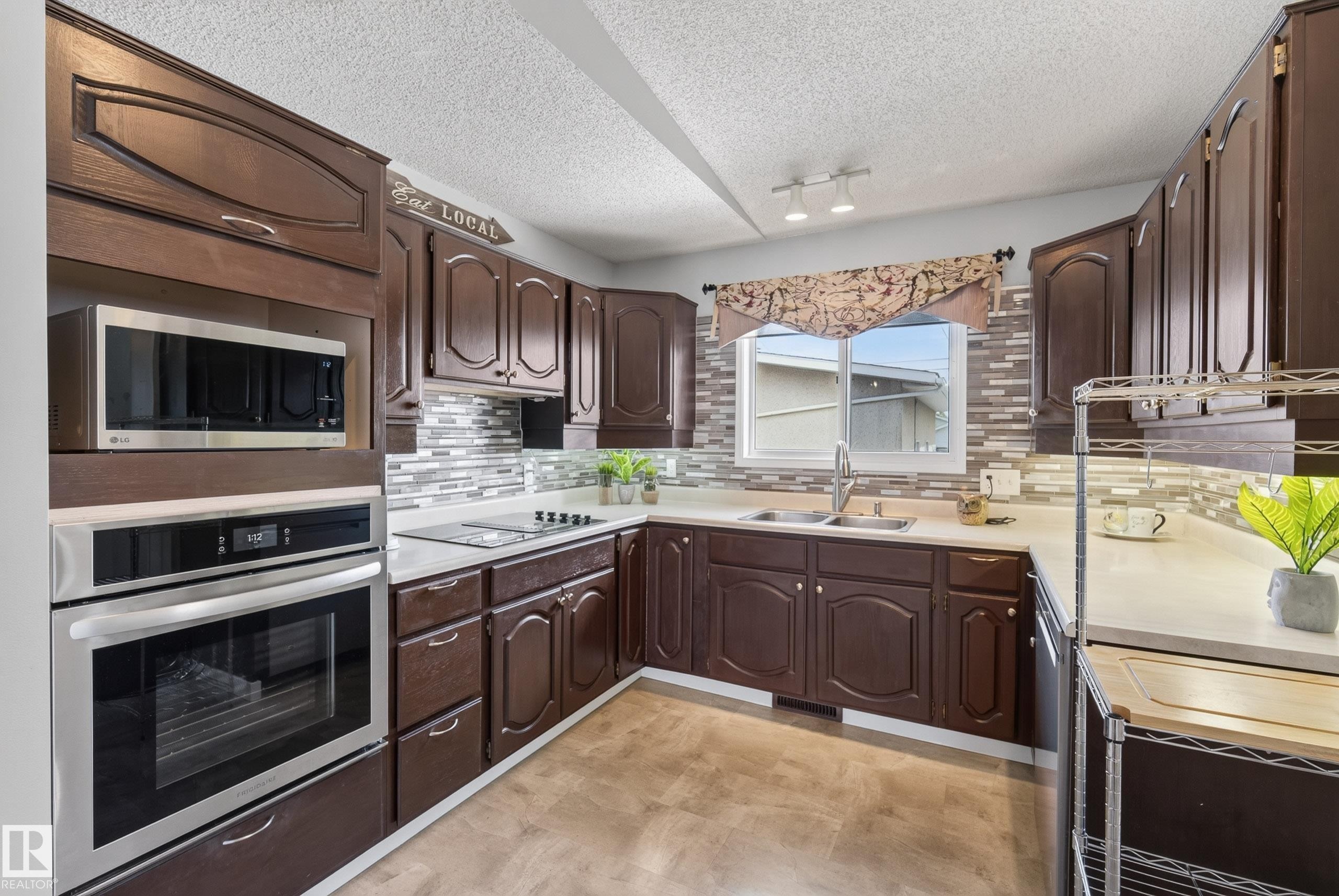 U-shaped kitchen with dark wood cabinetry, light countertops, and a full tile backsplash - 10935 152 Street, Edmonton, AB