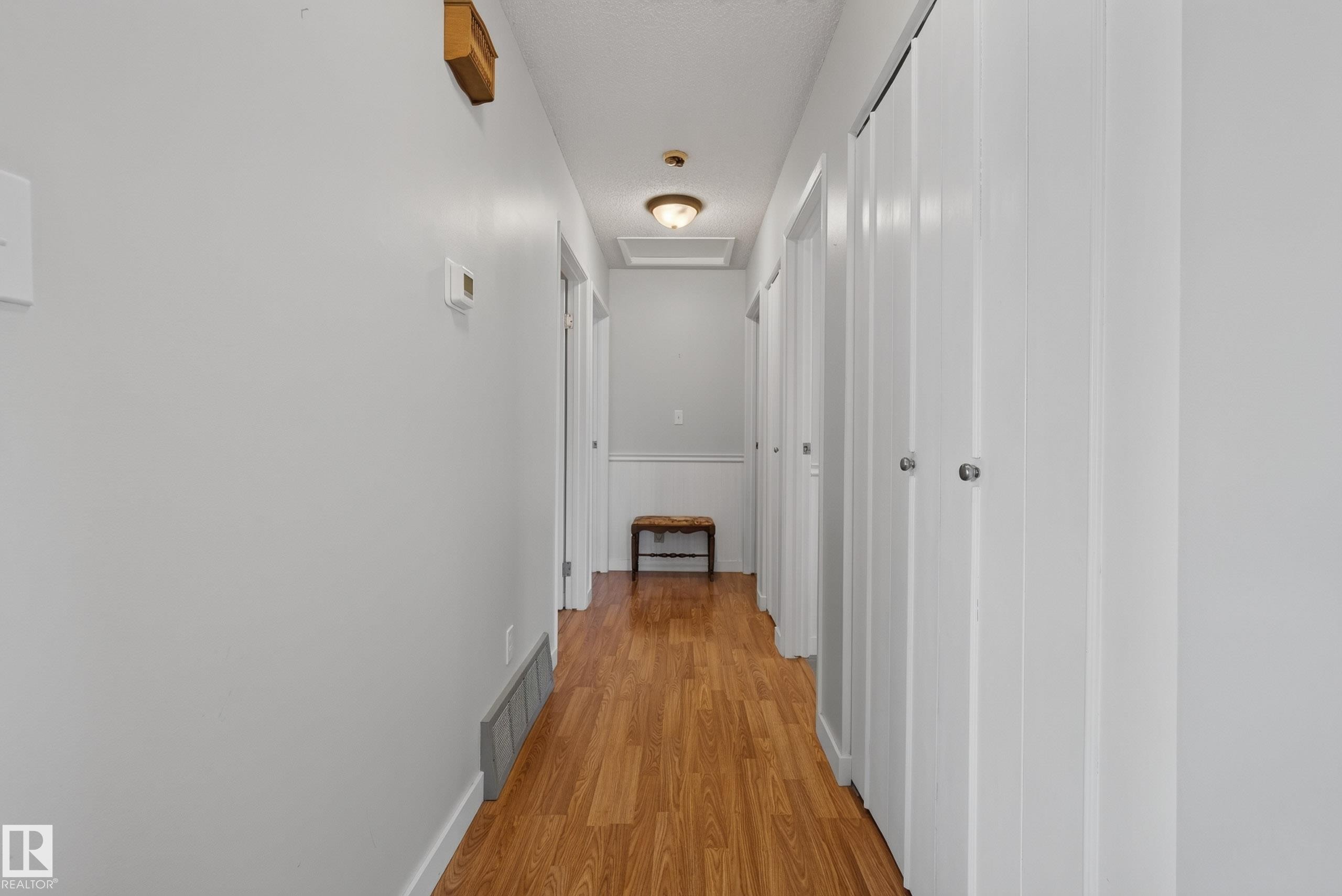 Hallway featuring wood-finish flooring, light gray wall paint, and multiple white bi-fold doors with round silver hardware - 10935 152 Street, Edmonton, AB