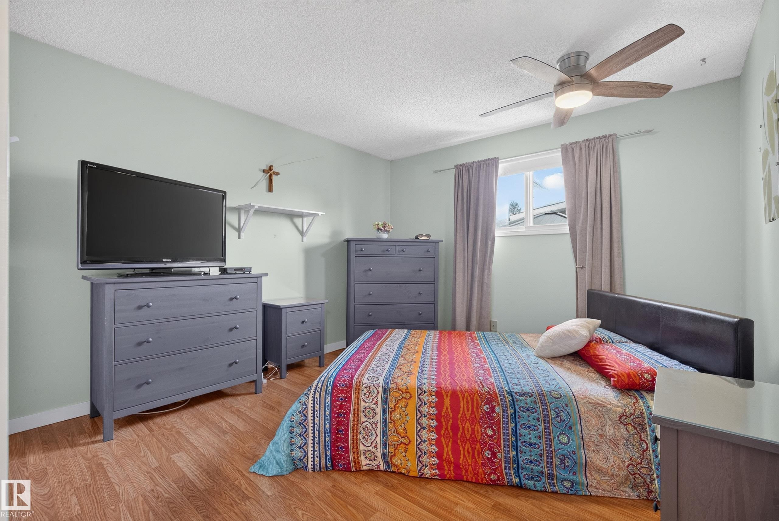 Bedroom featuring wood-finish flooring, a contemporary ceiling fan with integrated lighting, and a window with natural light - 10935 152 Street, Edmonton, AB