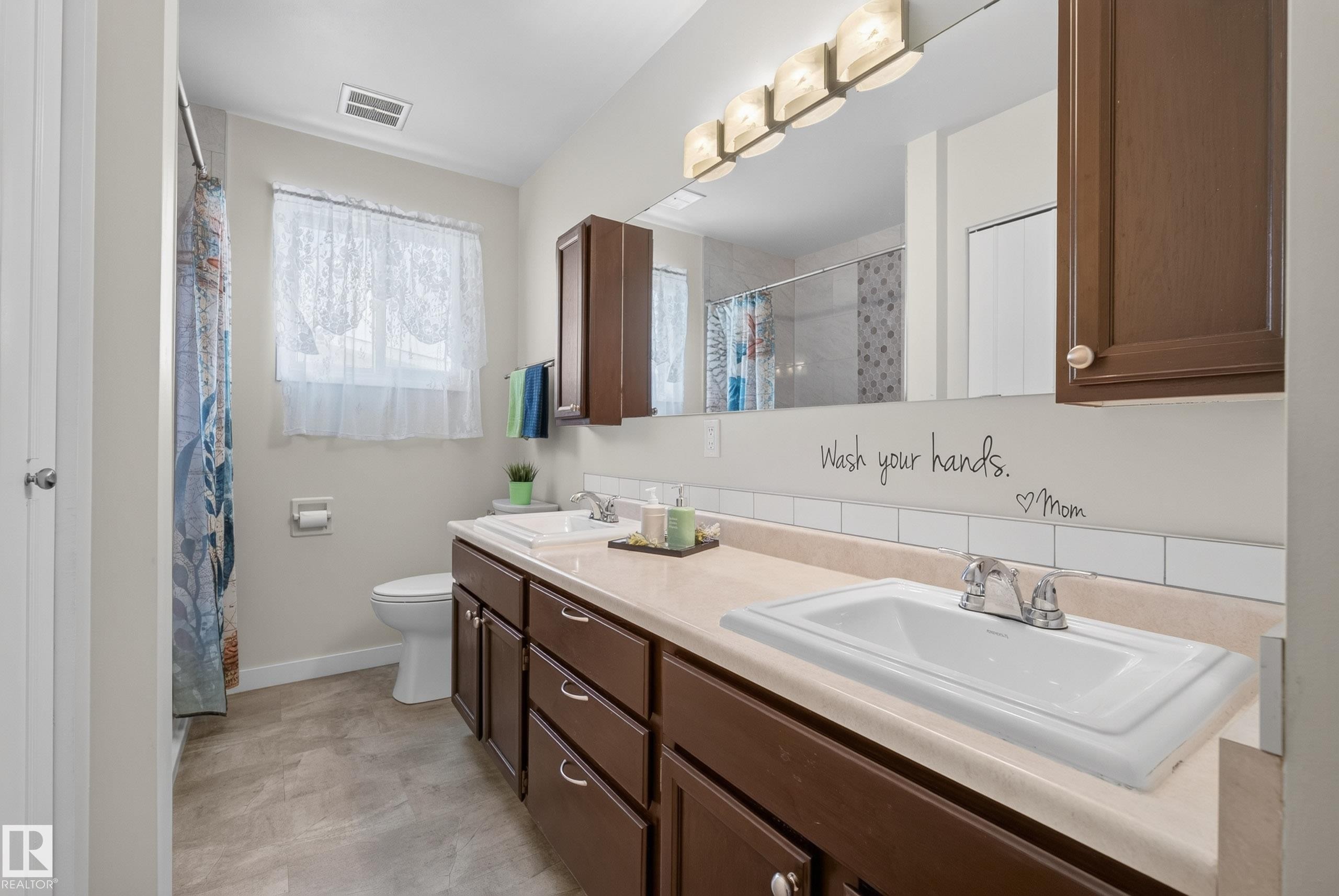 Bathroom featuring a double vanity with ample storage cabinetry, a toilet, and a shower with a privacy curtain - 10935 152 Street, Edmonton, AB