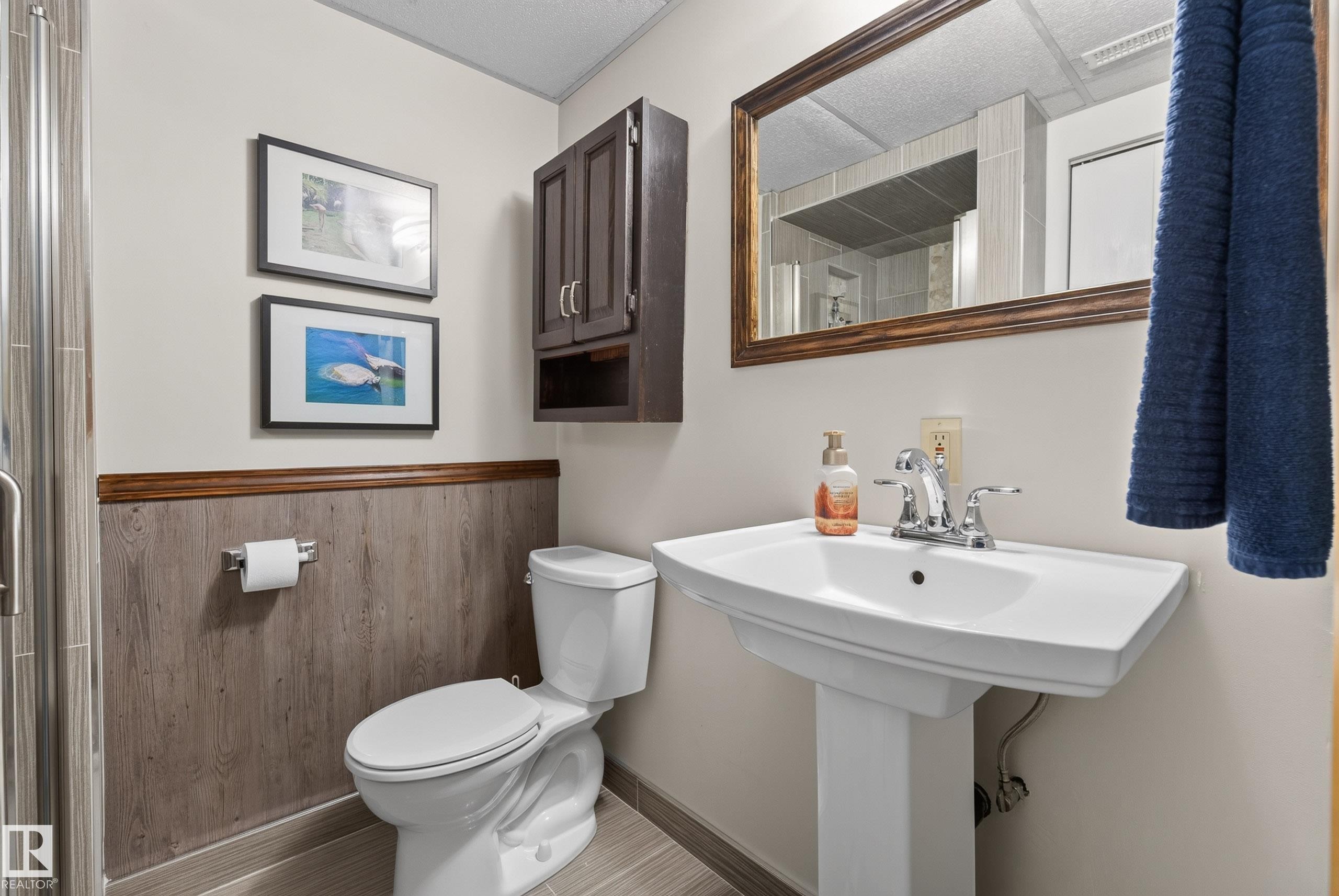 Bathroom featuring a pedestal sink with chrome faucet, wood-finish flooring, and wainscoting - 10935 152 Street, Edmonton, AB