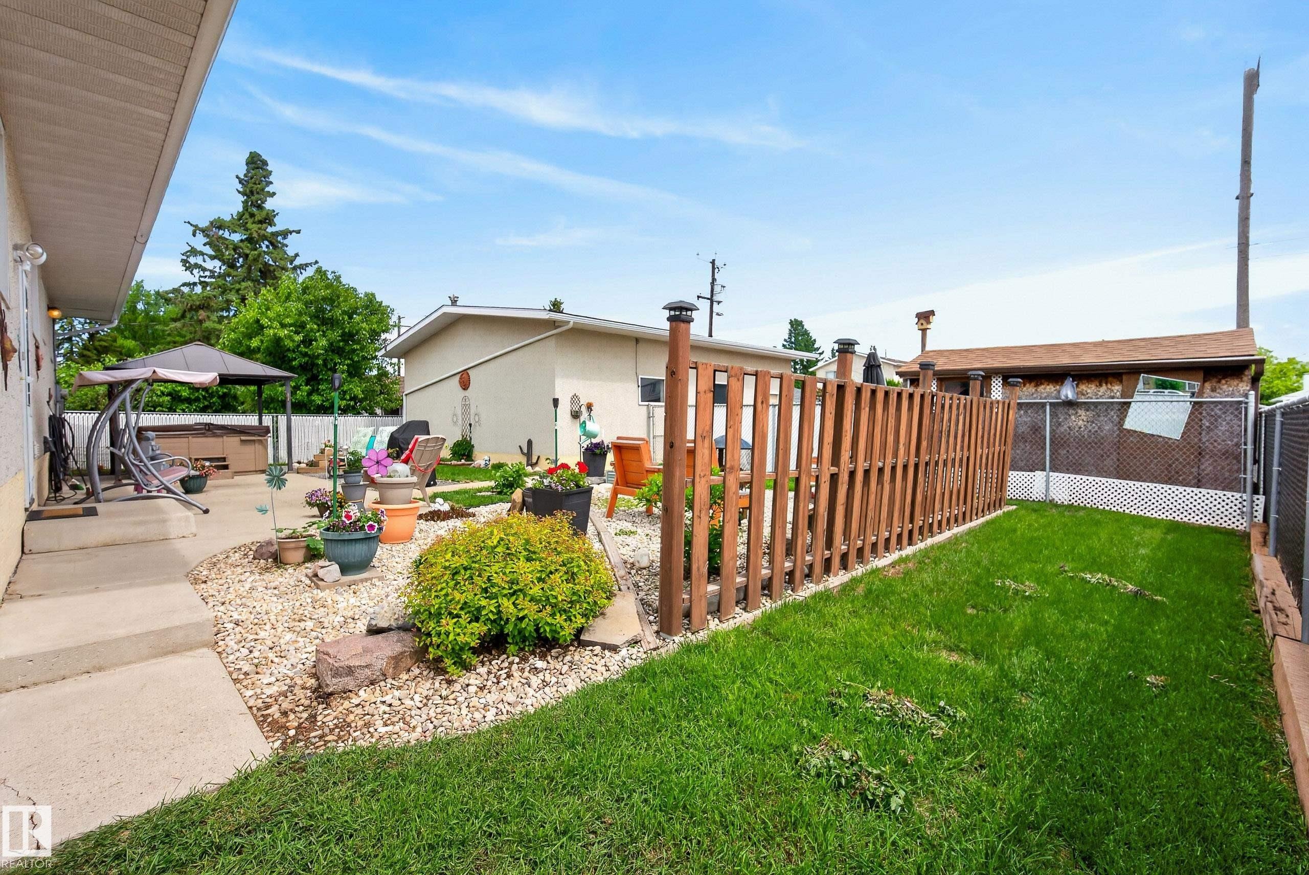 Expansive backyard featuring a manicured lawn, concrete patio, a gravel landscape bed, and a vertical wood-slat privacy fence - 10935 152 Street, Edmonton, AB
