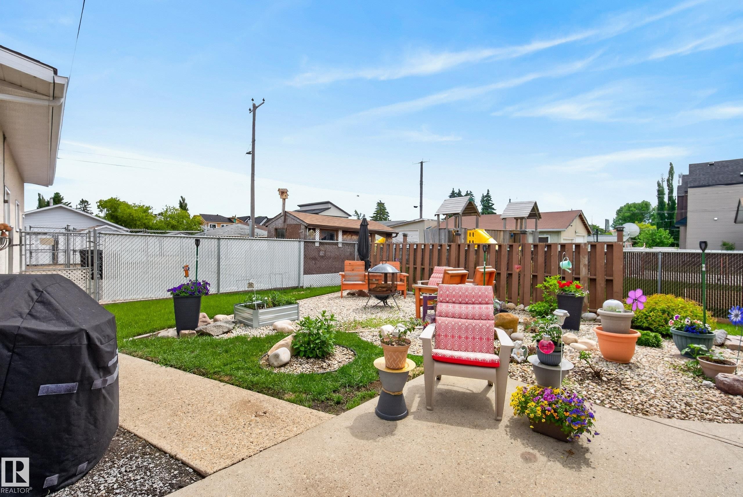 Spacious backyard featuring a concrete patio, landscaped garden beds with decorative rocks, a raised garden planter, and a wood fence boundary - 10935 152 Street, Edmonton, AB