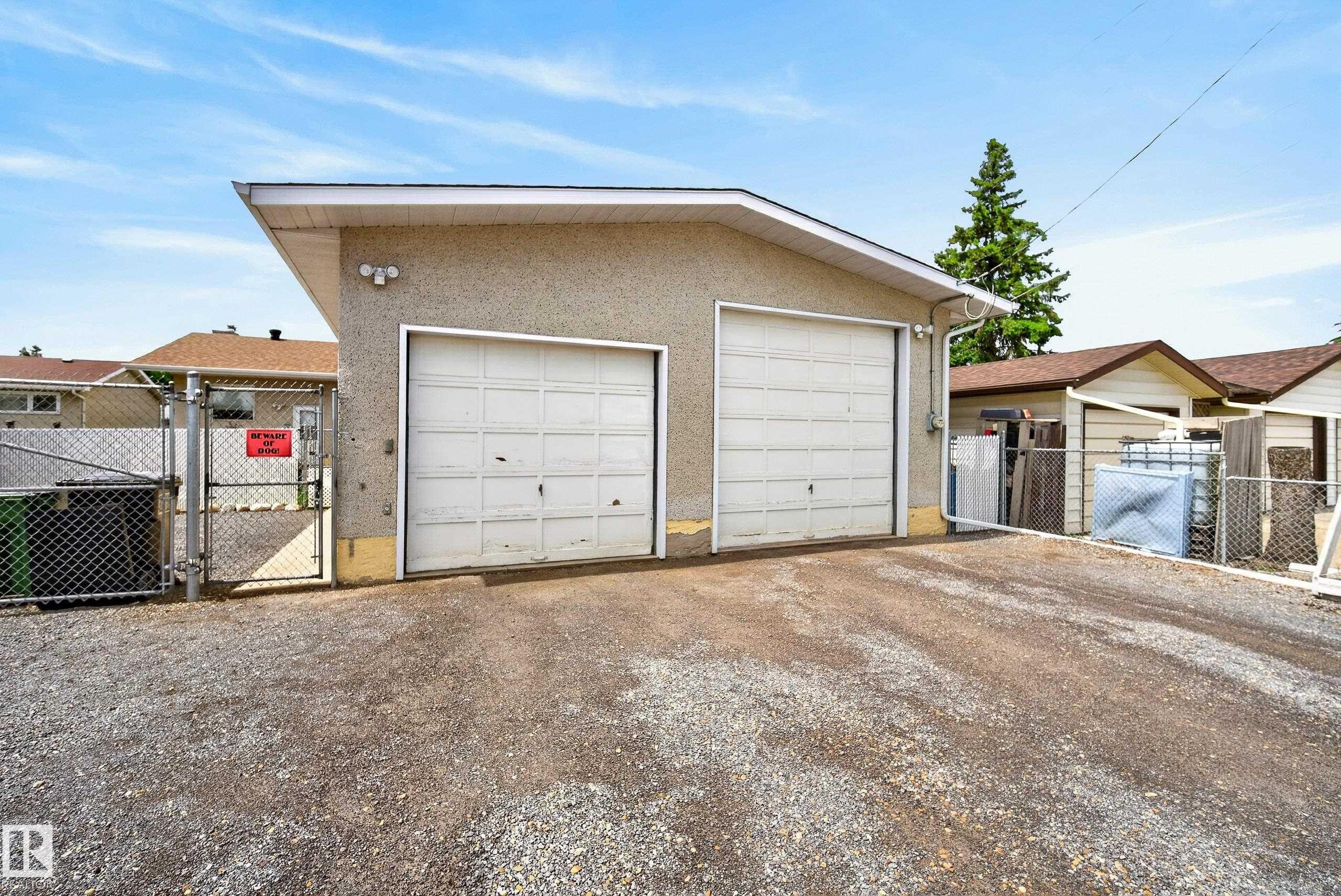Detached two-car garage with two white panel garage doors, stucco exterior, and a gravel driveway - 10935 152 Street, Edmonton, AB