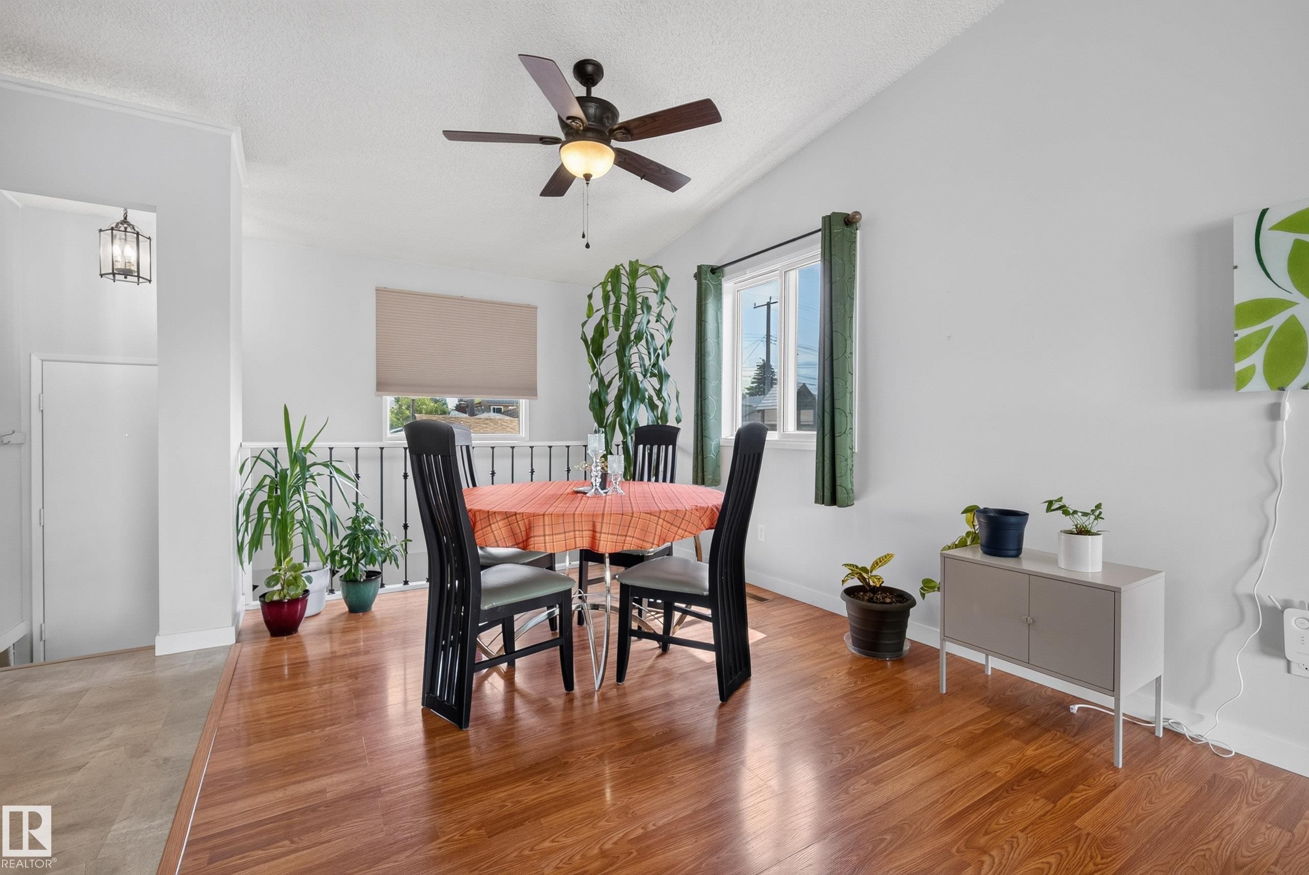 Open concept dining area featuring wood-finish flooring, a ceiling fan with integrated lighting, and a window with a roller blind - 10935 152 Street, Edmonton, AB