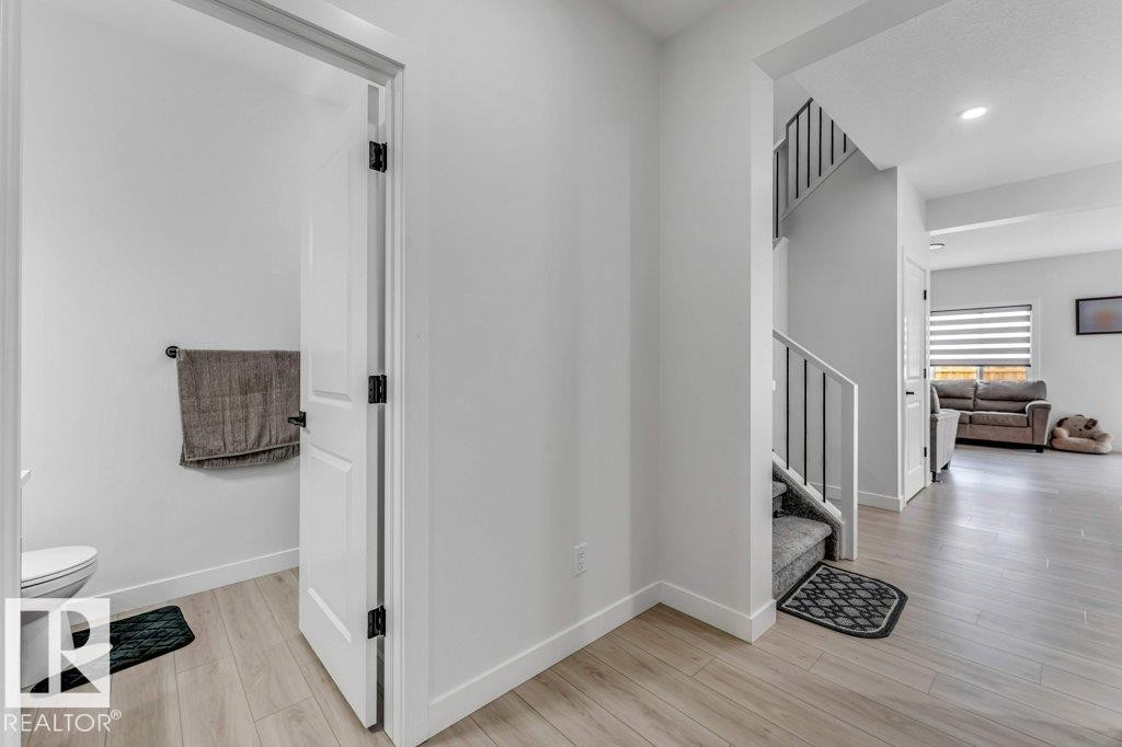 Bright hallway with wood-finish flooring, a white interior door with black hardware, and a staircase featuring carpeted treads and black metal balusters - 423 28 Street, Edmonton, AB