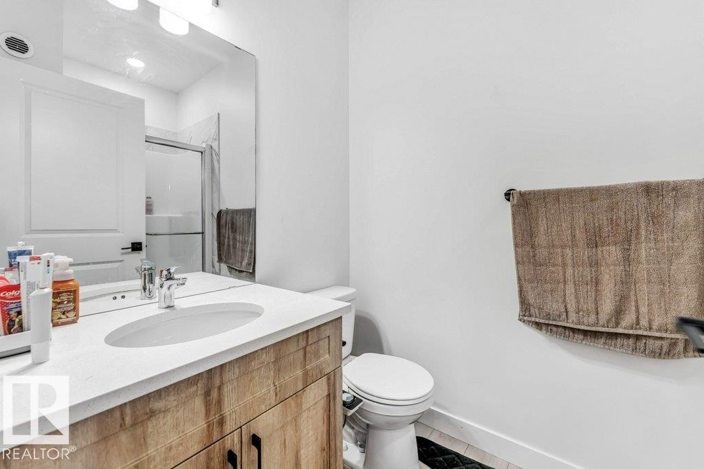 Modern bathroom featuring a wood-finish vanity with an integrated white sink, chrome faucet, and a large wall-mounted mirror - 423 28 Street, Edmonton, AB