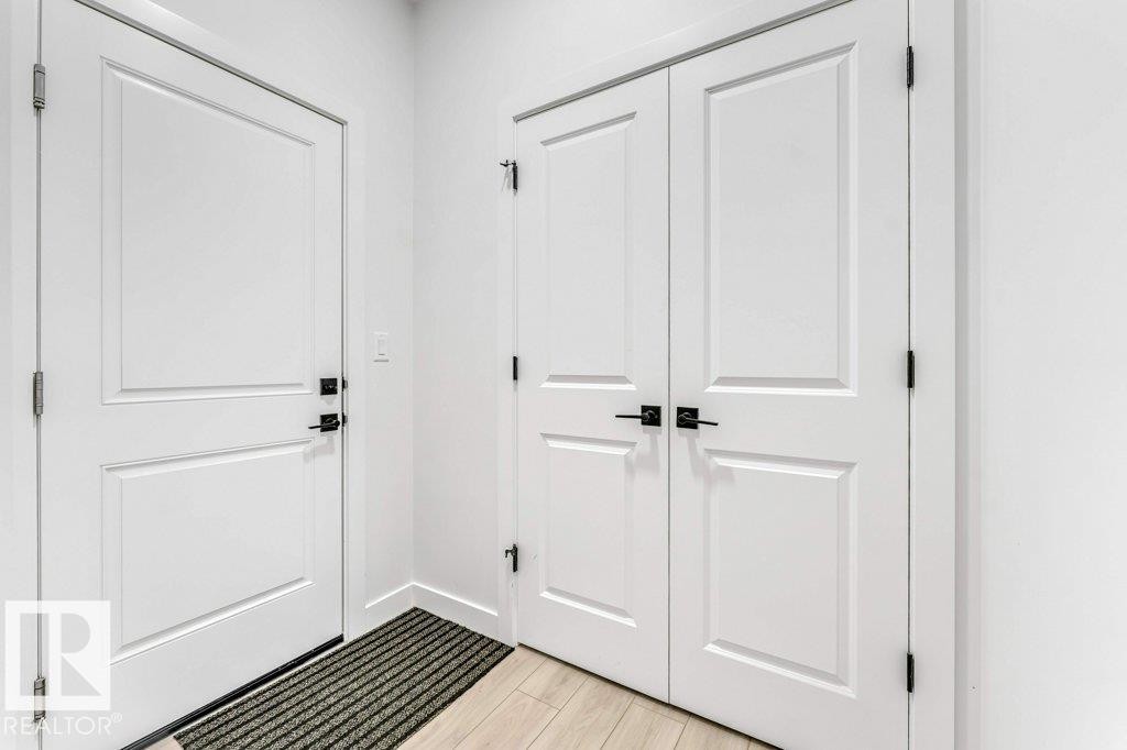 Entryway featuring light wood-finish flooring, white paneled doors, and matte black hardware - 423 28 Street, Edmonton, AB