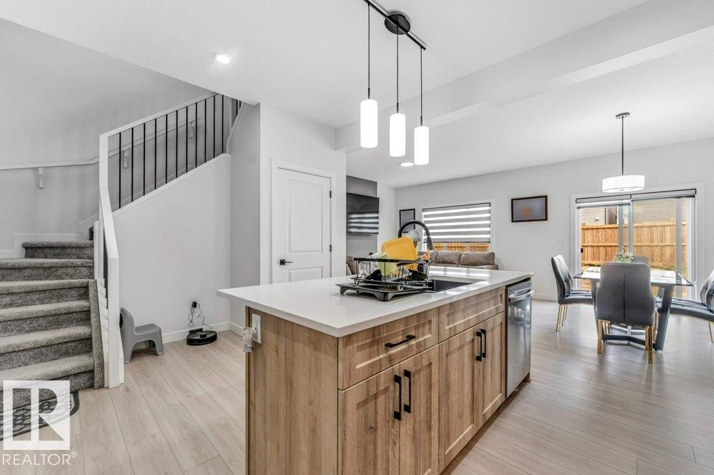 Open-concept layout featuring a kitchen island with light wood-finish cabinetry, a white countertop, and pendant lighting - 423 28 Street, Edmonton, AB