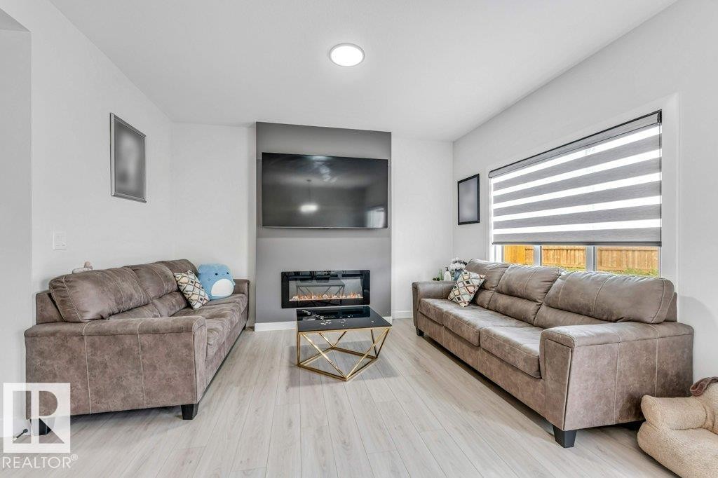 Bright living space featuring light wood-finish flooring, recessed lighting, and an accent wall with a built-in electric fireplace - 423 28 Street, Edmonton, AB
