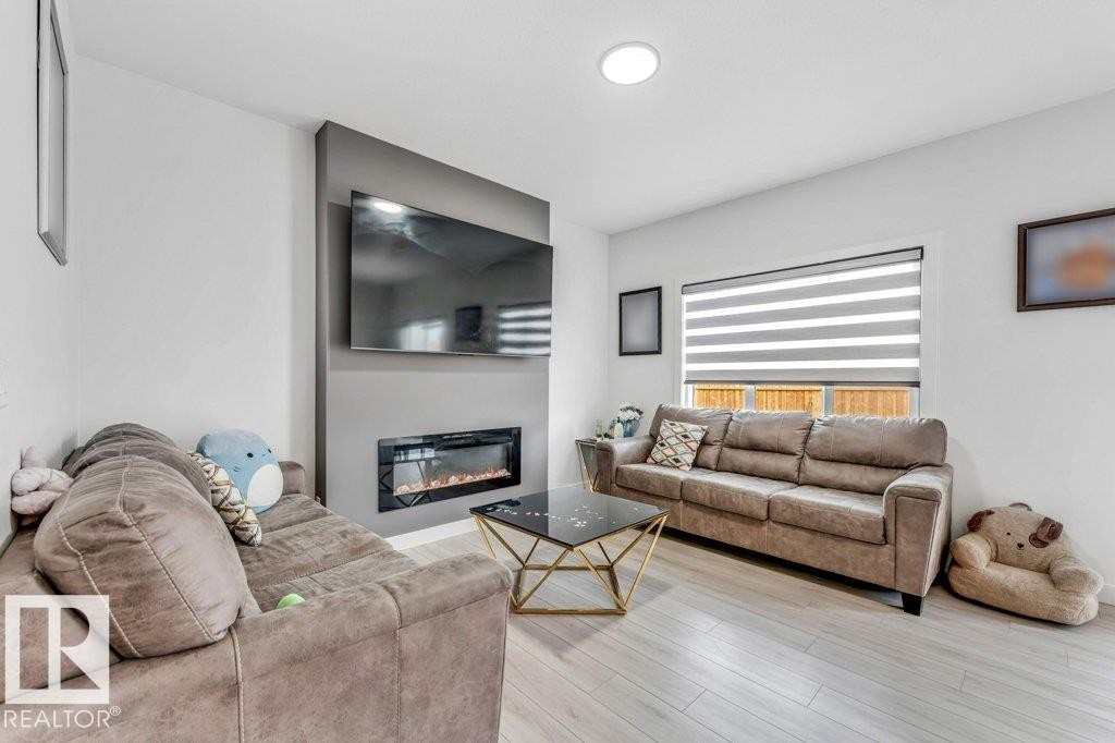 Living area featuring a modern electric fireplace with a dark surround, recessed ceiling lighting, and light wood-finish flooring - 423 28 Street, Edmonton, AB
